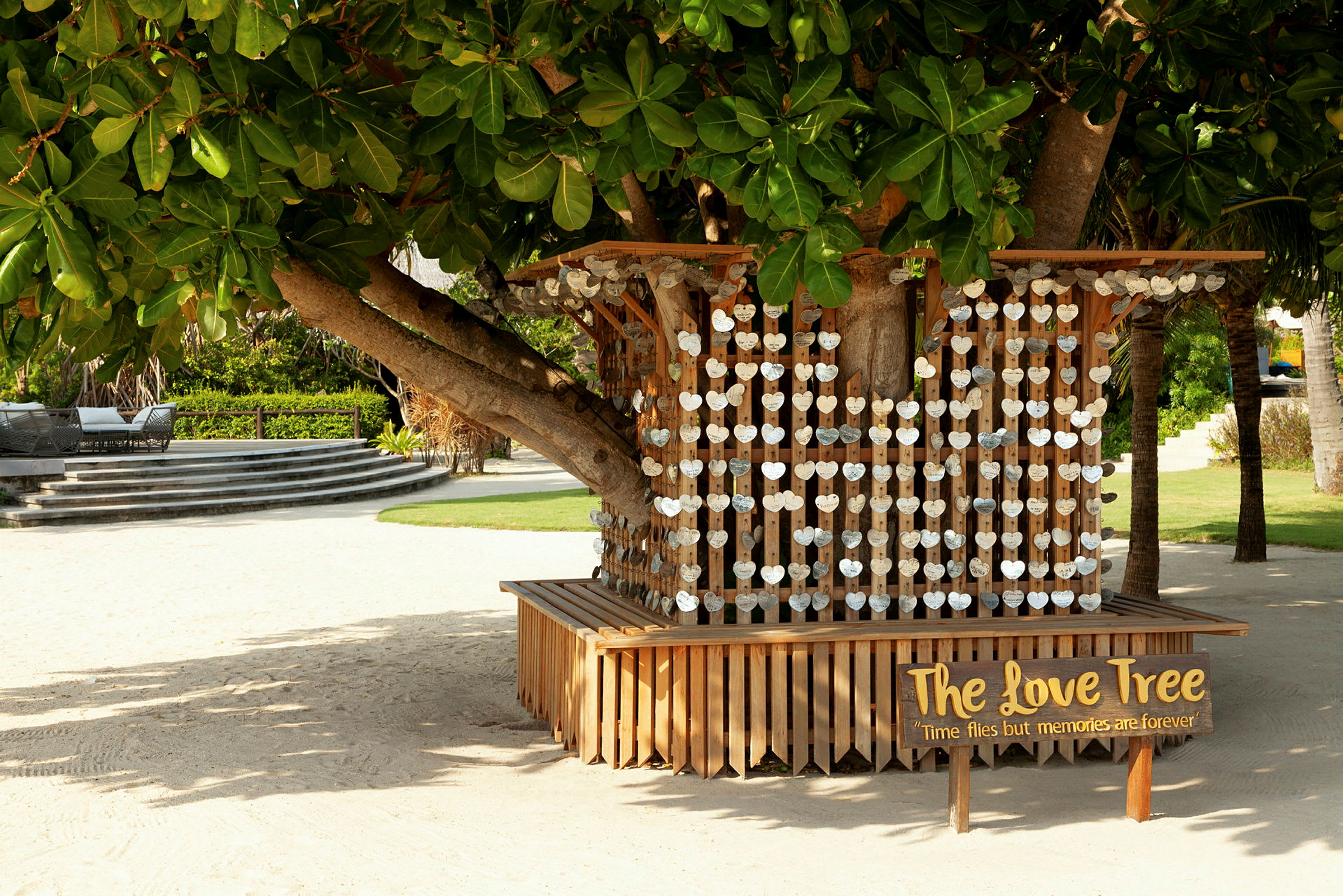 Et tre omgitt av en trekonstruksjon med hengende hjerteformede dekorasjoner. Et skilt ved siden av lyder 'The Love Tree'. (AI-generert tekst)