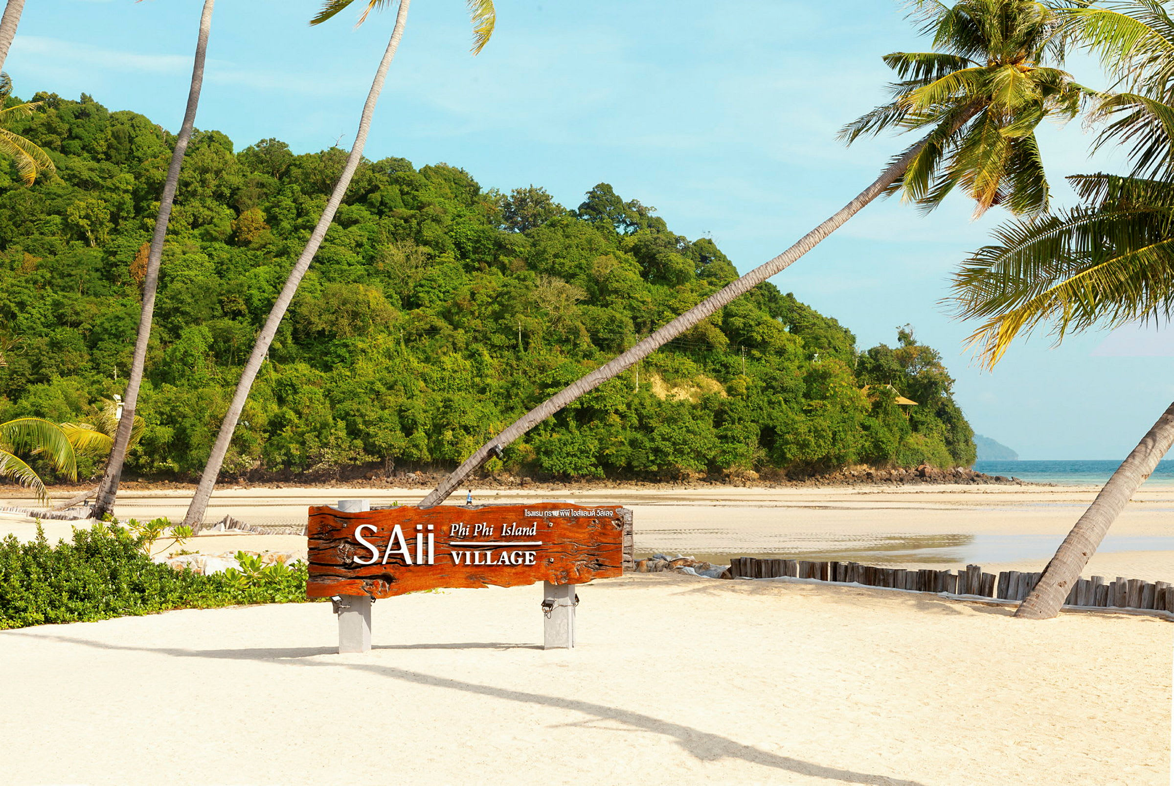 Sandstrand med palmer og et tregilt som lyder "SAii Phi Phi Island Village", med grønn vegetasjon og havet i bakgrunnen. (AI-generert tekst)