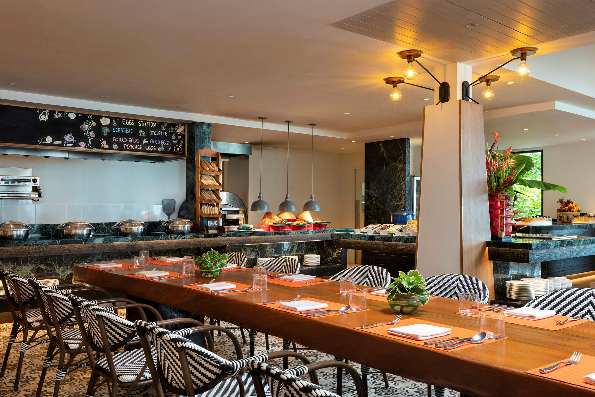 Interiør av en restaurant med et langbord, stoler med mønstrede seter og en frokostbuffet med mat og dekorasjoner. (AI-generert tekst)