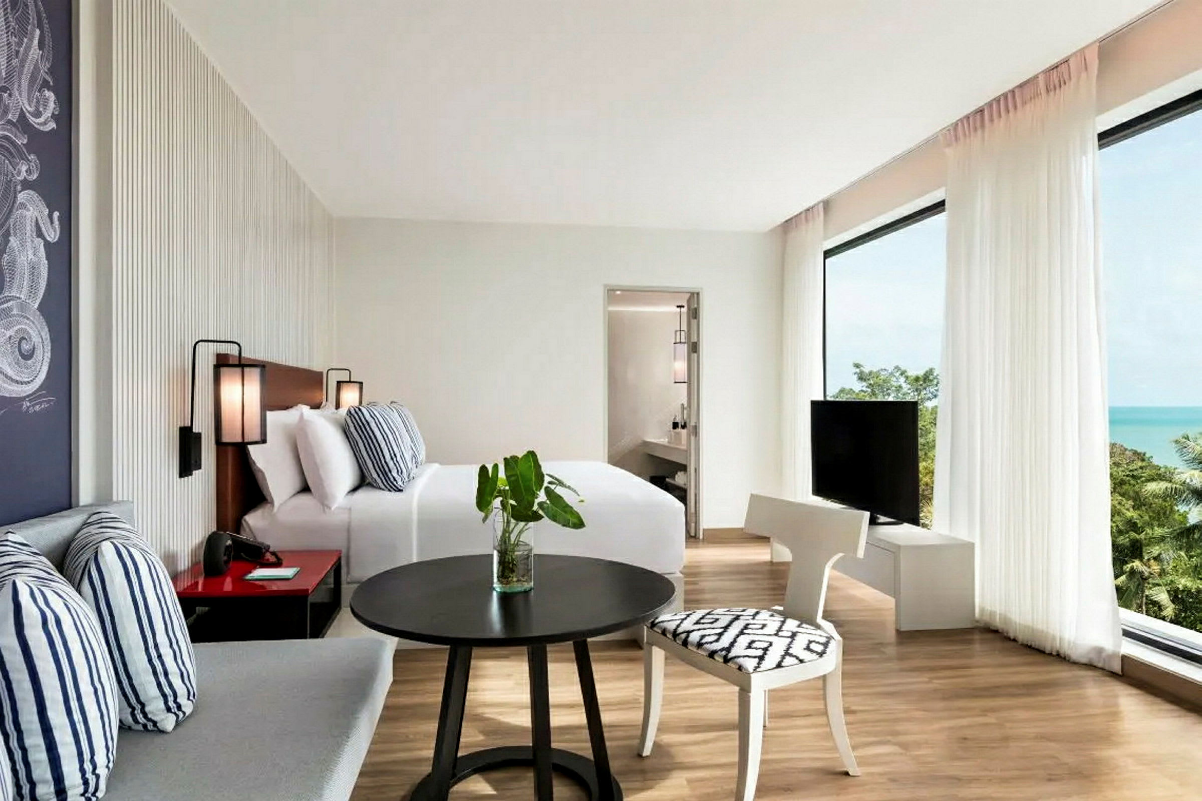 Et lyst hotellrom med seng, sittegruppe, TV og utsikt over havet. (AI-generert tekst)