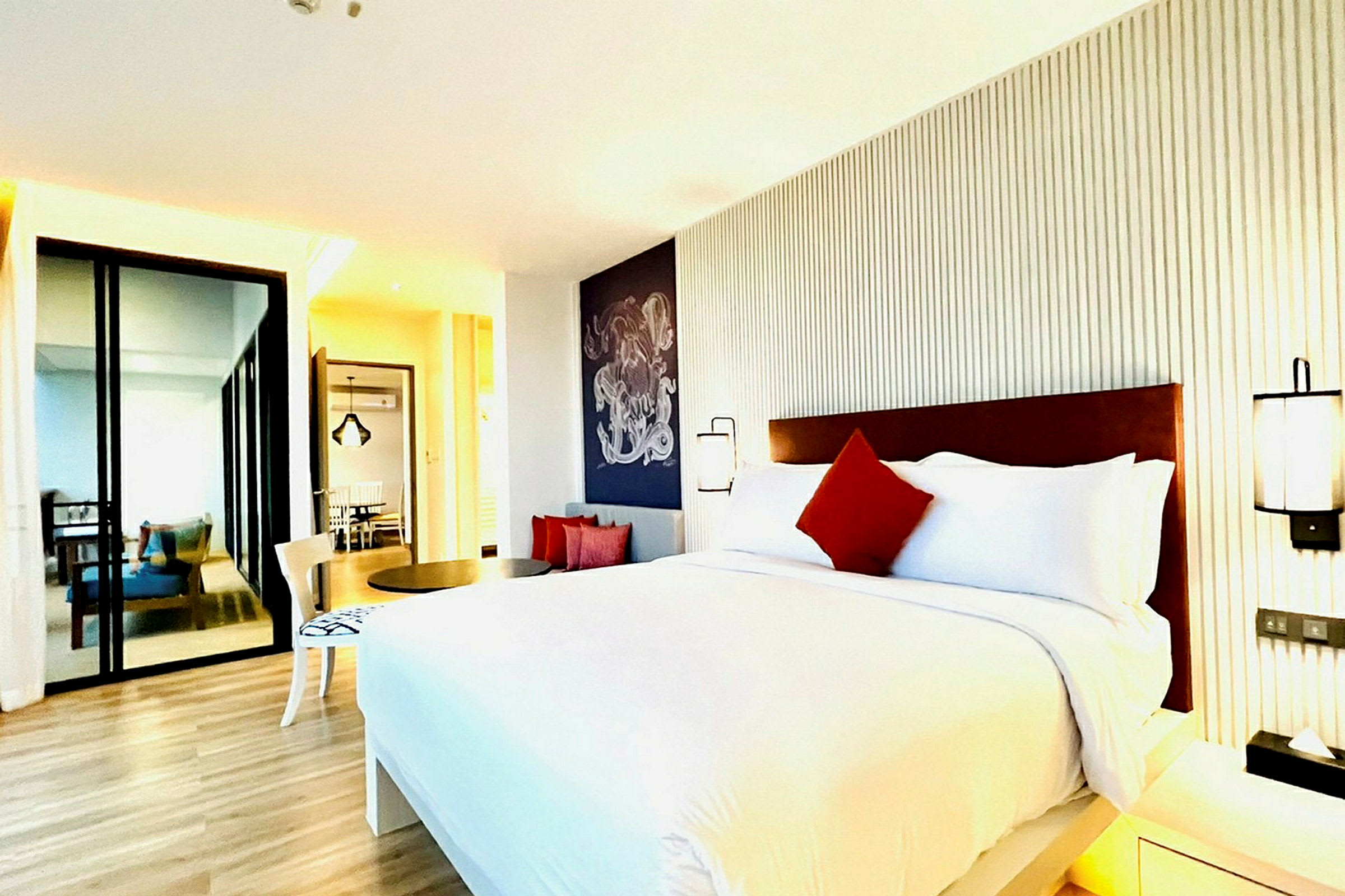 Et moderne hotellrom med en stor seng, hvite og røde puter, minimalistisk innredning og tregulv. (AI-generert tekst)