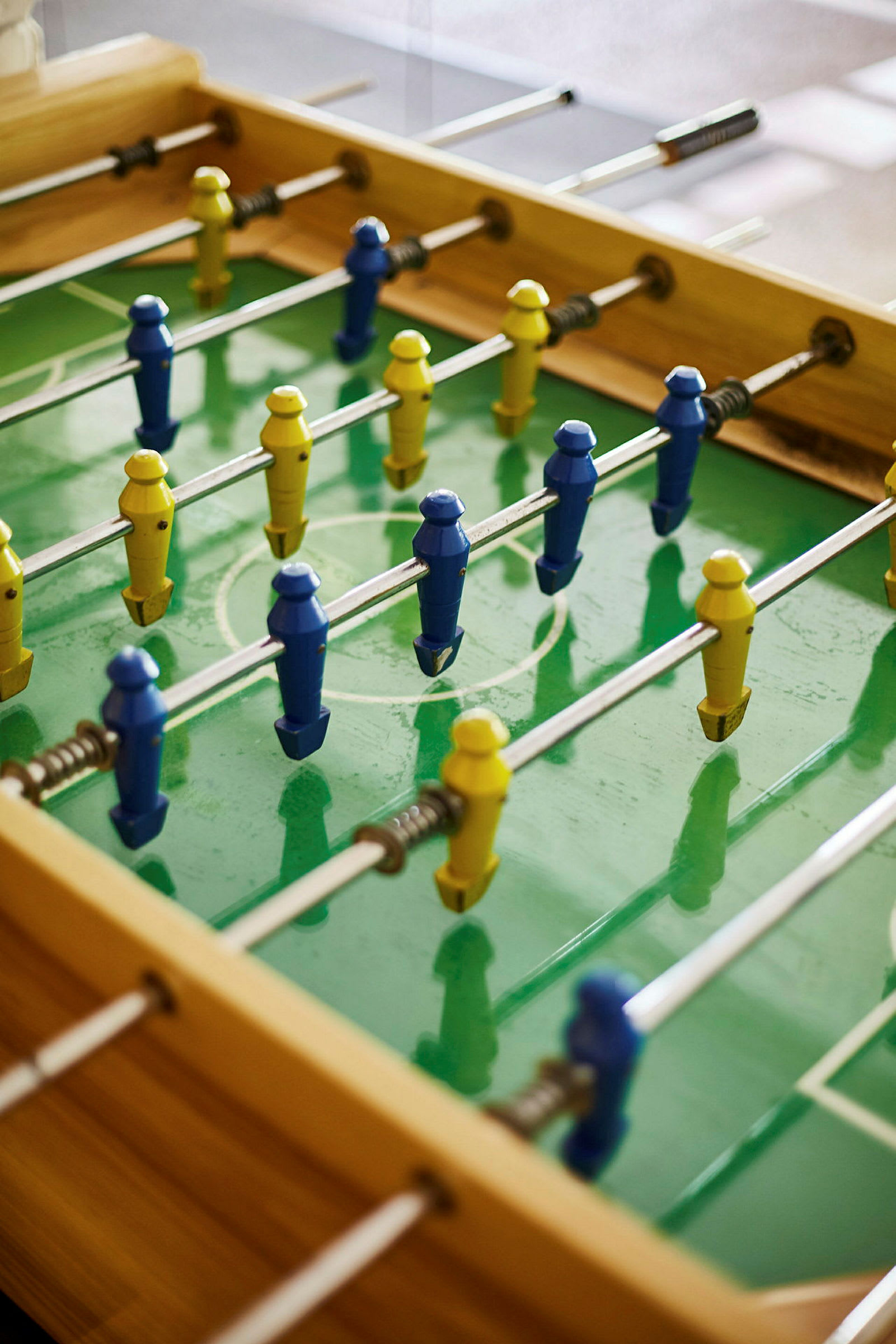 En bordfotballbane med plastfigurer i blå og gul farge på en grønn spilleflate. (AI-generert tekst)