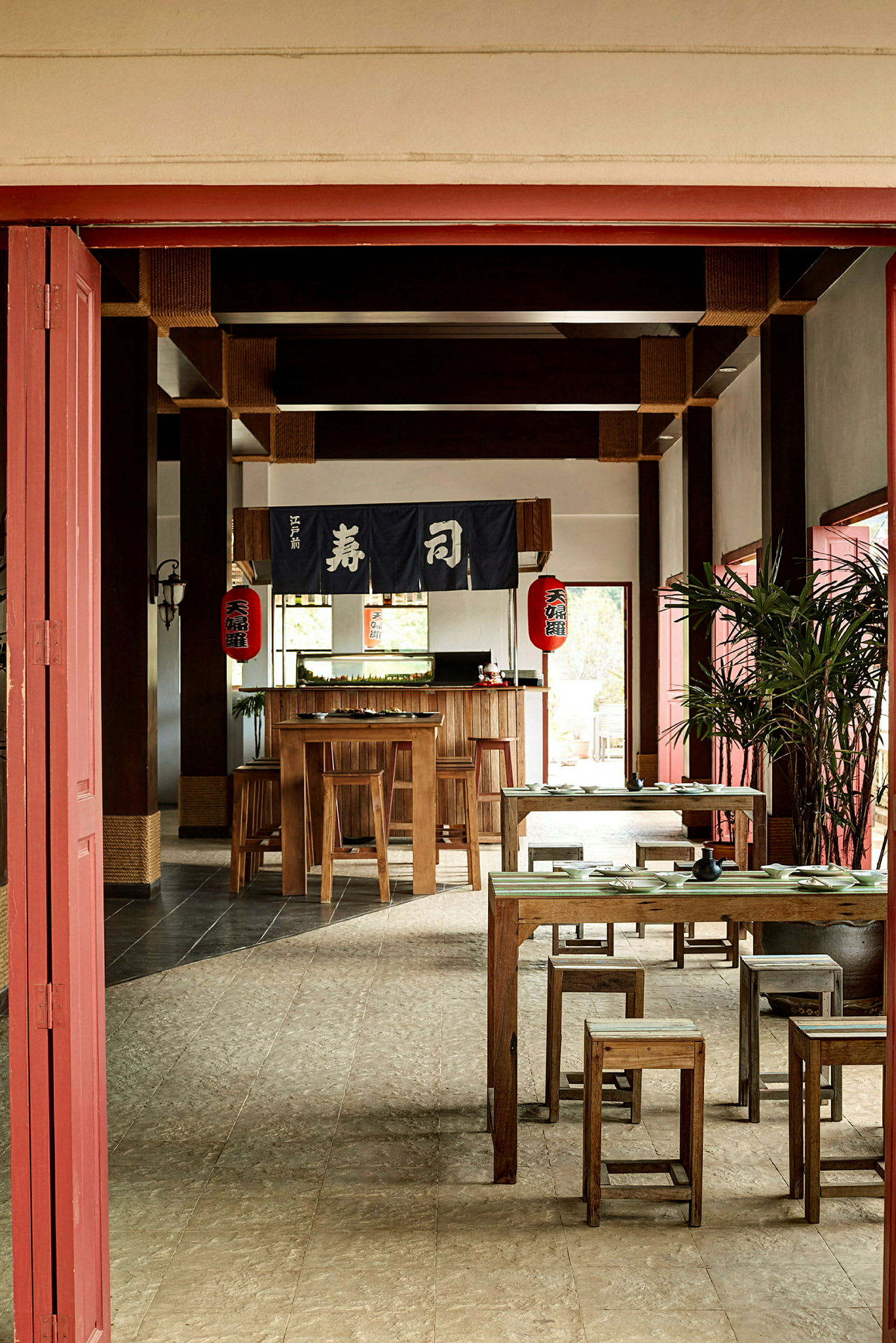 Et rom innredet som en japansk restaurant med trebord og stoler, dekorert med japanske lykter og tekstil med japanske tegn. (AI-generert tekst)