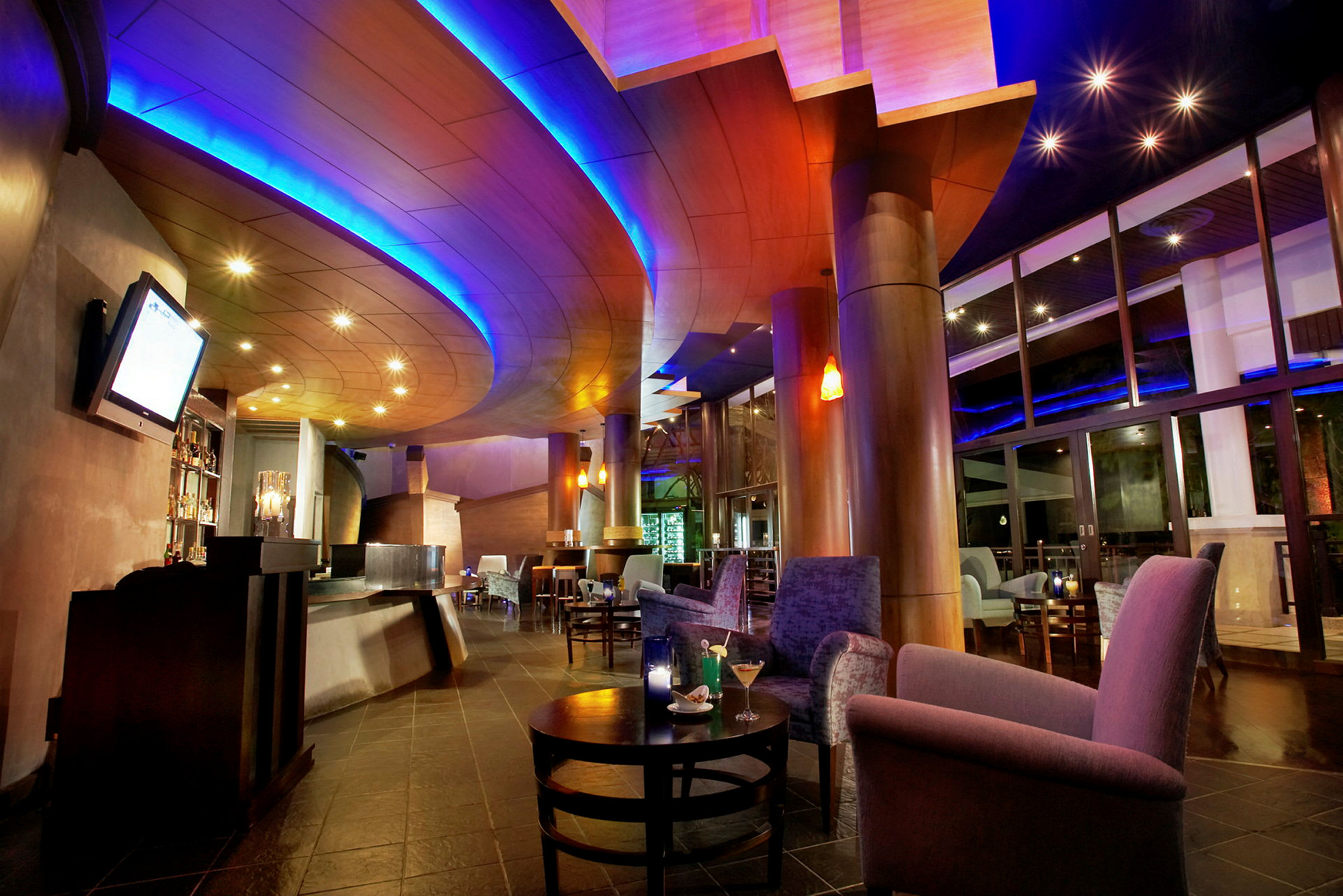 Et interiør av en moderne lounge eller bar med en buet takdesign, myke lenestoler og sofaer, samt stilfull belysning i rommet. (AI-generert tekst)