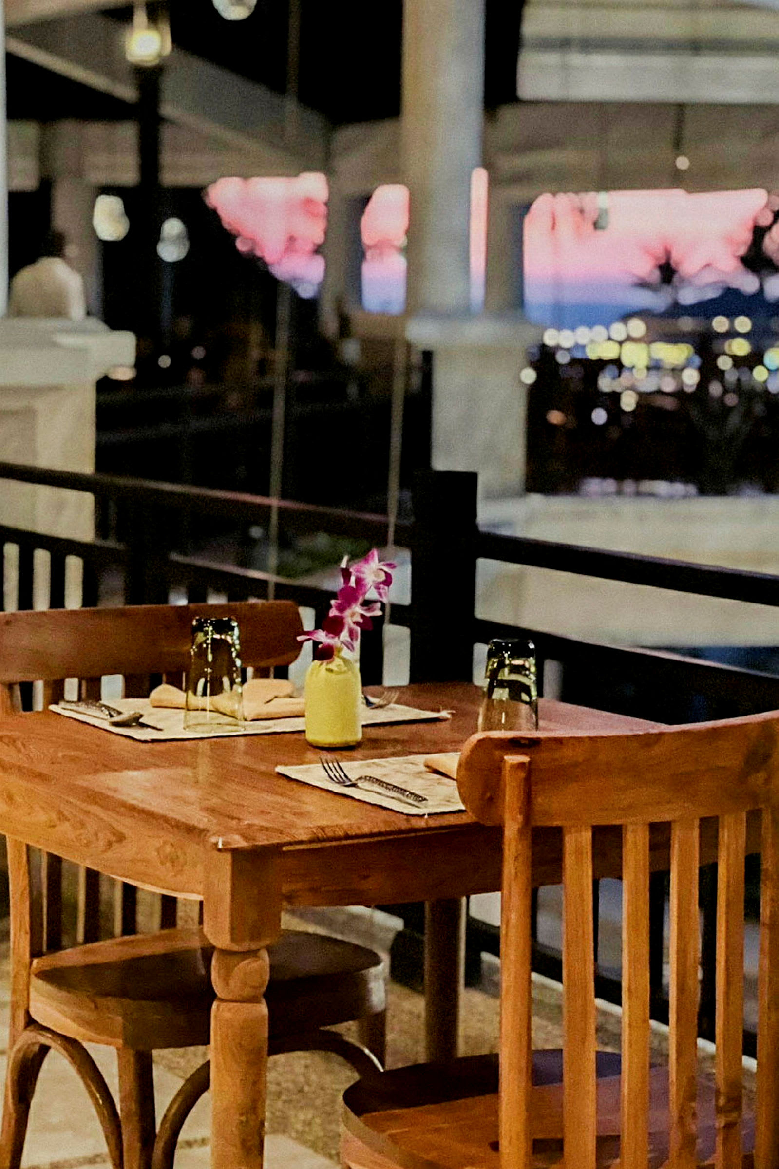Et dekket trebord med to stoler ved en restaurantterrasse og bakgrunn med uskarpt utsikt over kveldslandskap. (AI-generert tekst)