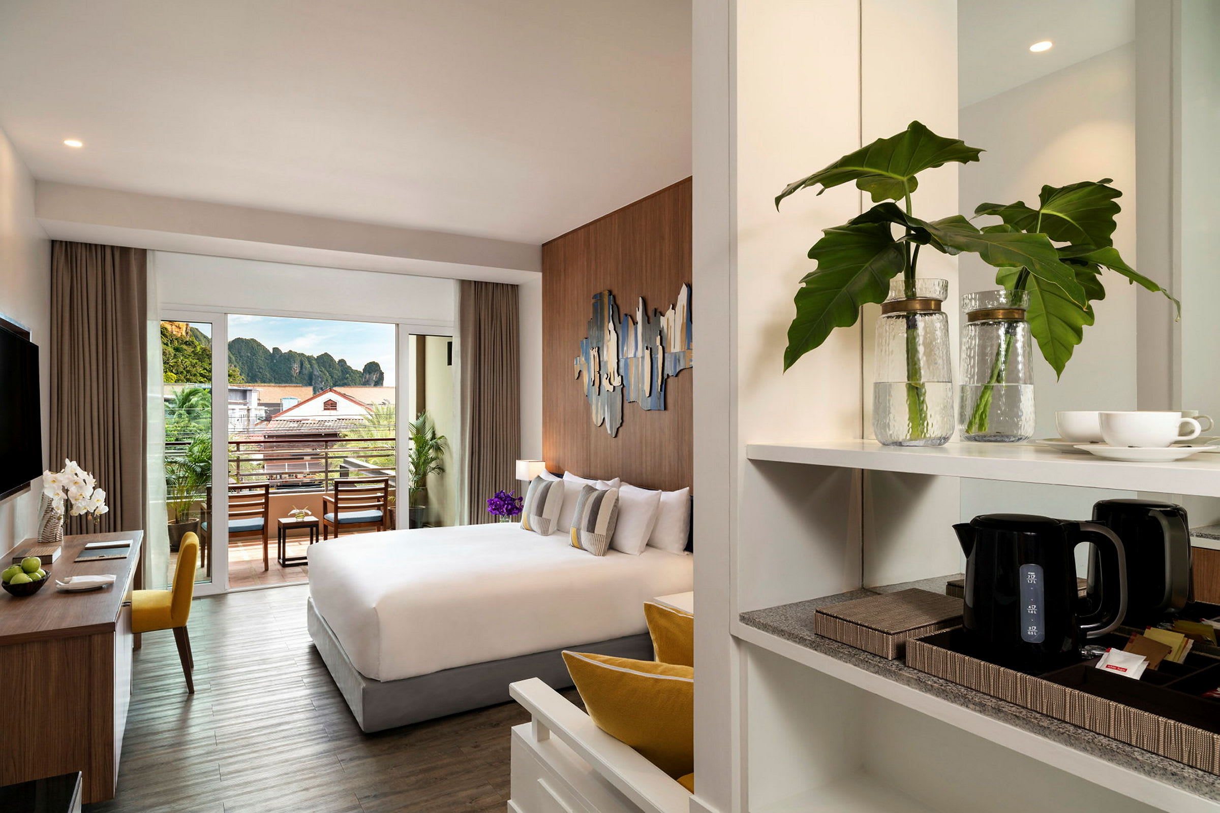 Et moderne hotellrom med en komfortabel seng, arbeidsområde og en balkong med utsikt over omgivelsene. (AI-generert tekst)