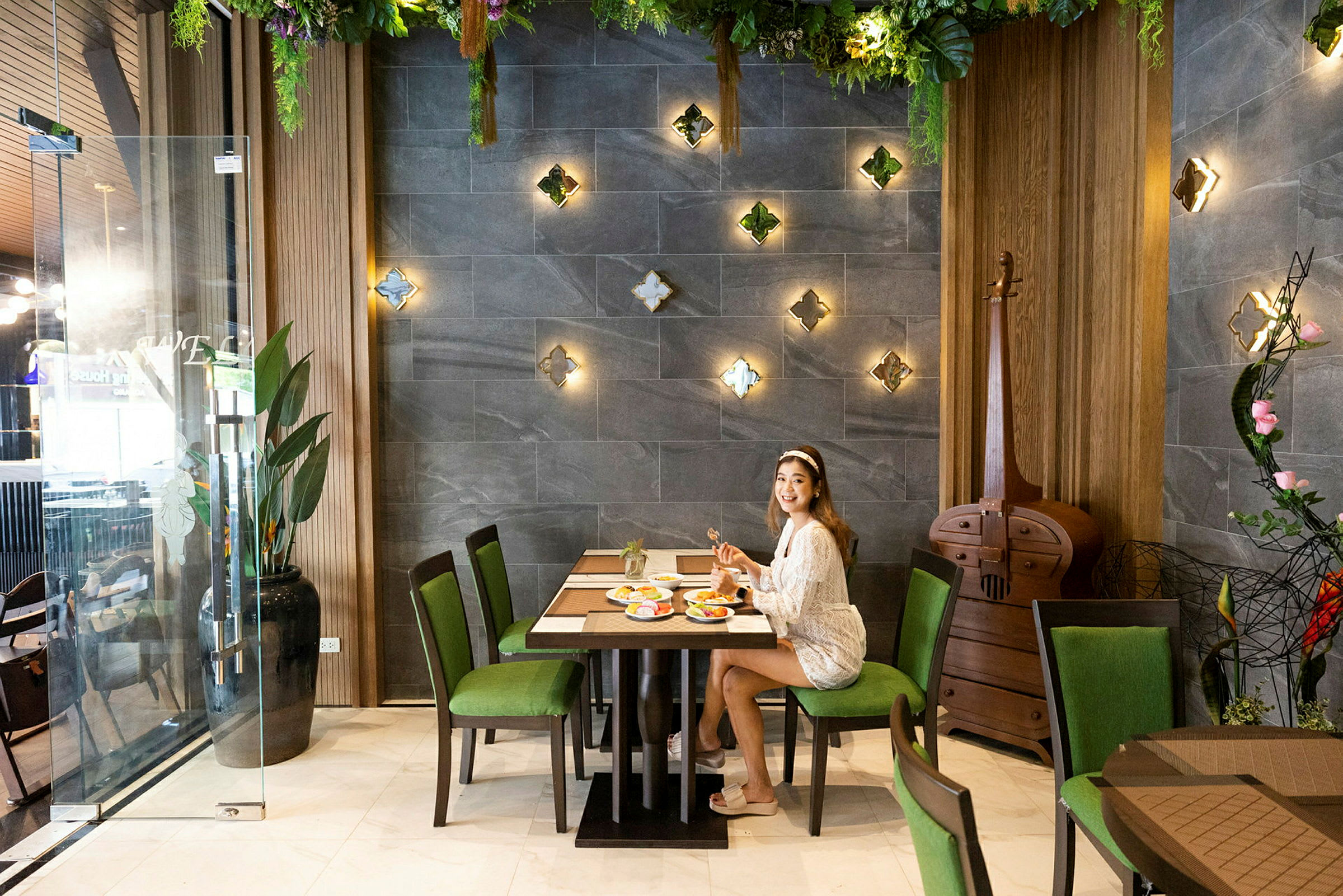 Person sitter ved et bord på en restaurant med veggdekorasjoner og frodig interiør. (AI-generert tekst)
