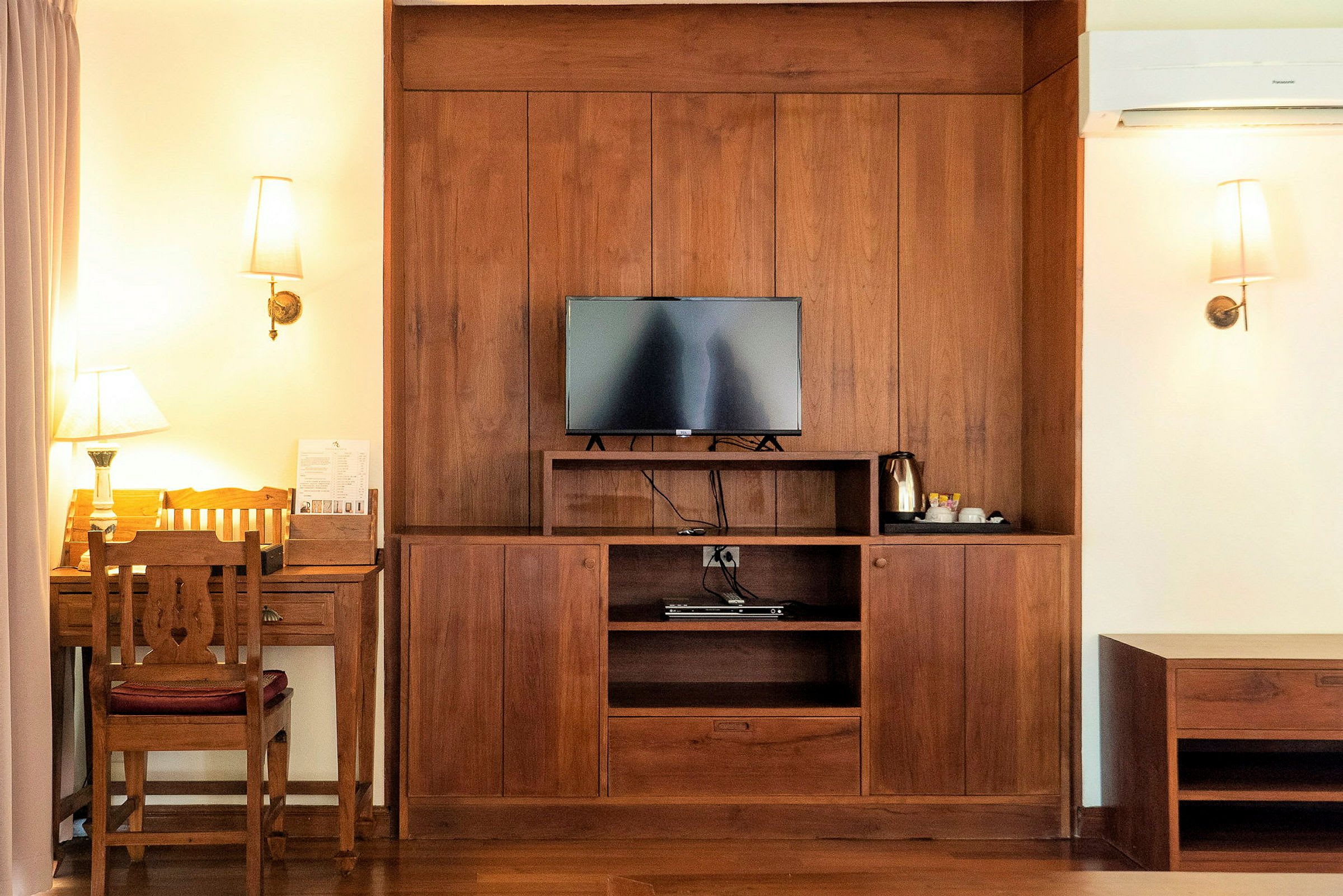 Interiørbilde av et hotellrom med en trepanel hvor en TV, en kaffetrakter og et skrivebord med stol er plassert. (AI-generert tekst)
