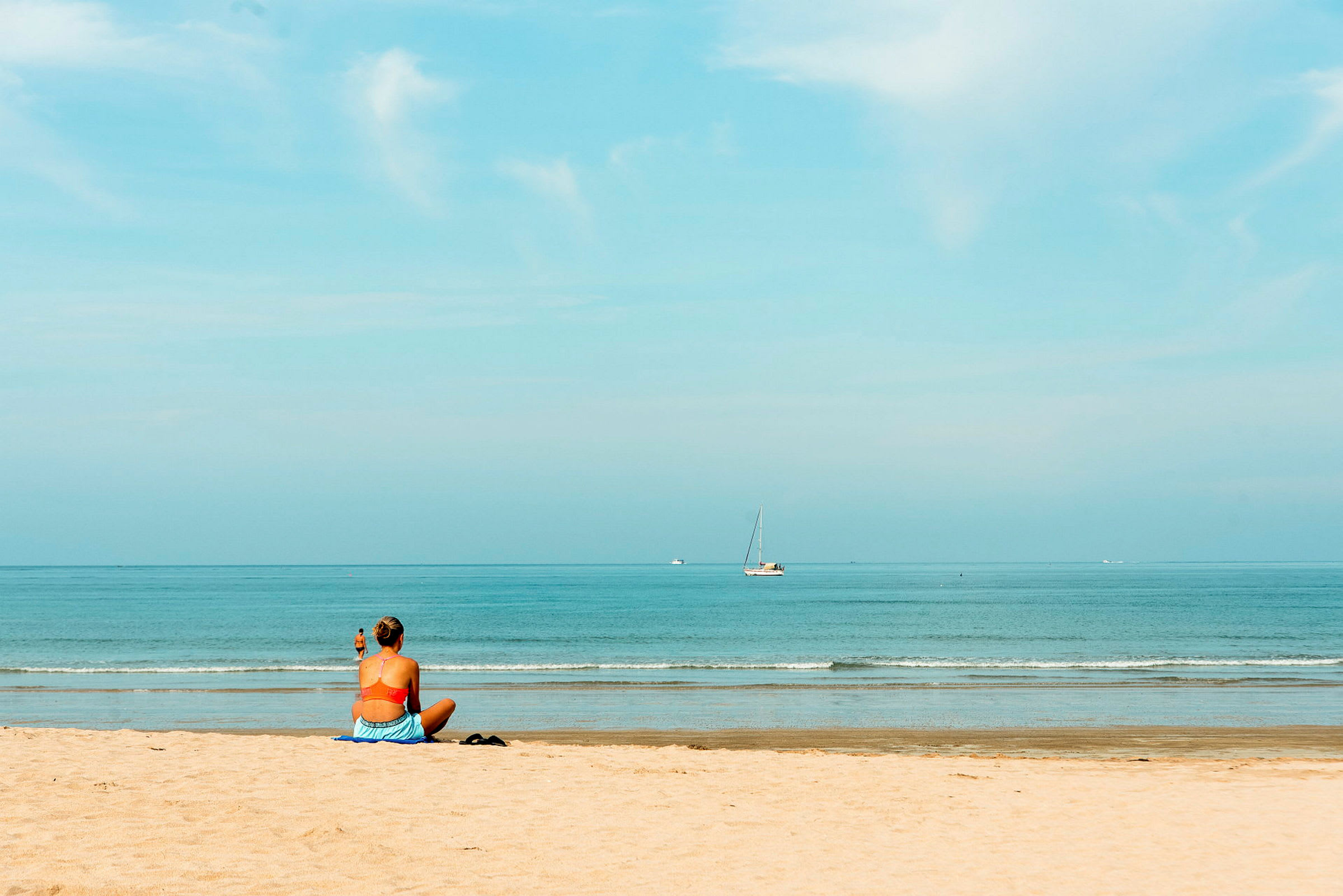 En person sitter på en strand og ser utover havet, der en seilbåt er synlig i det fjerne. (AI-generert tekst)