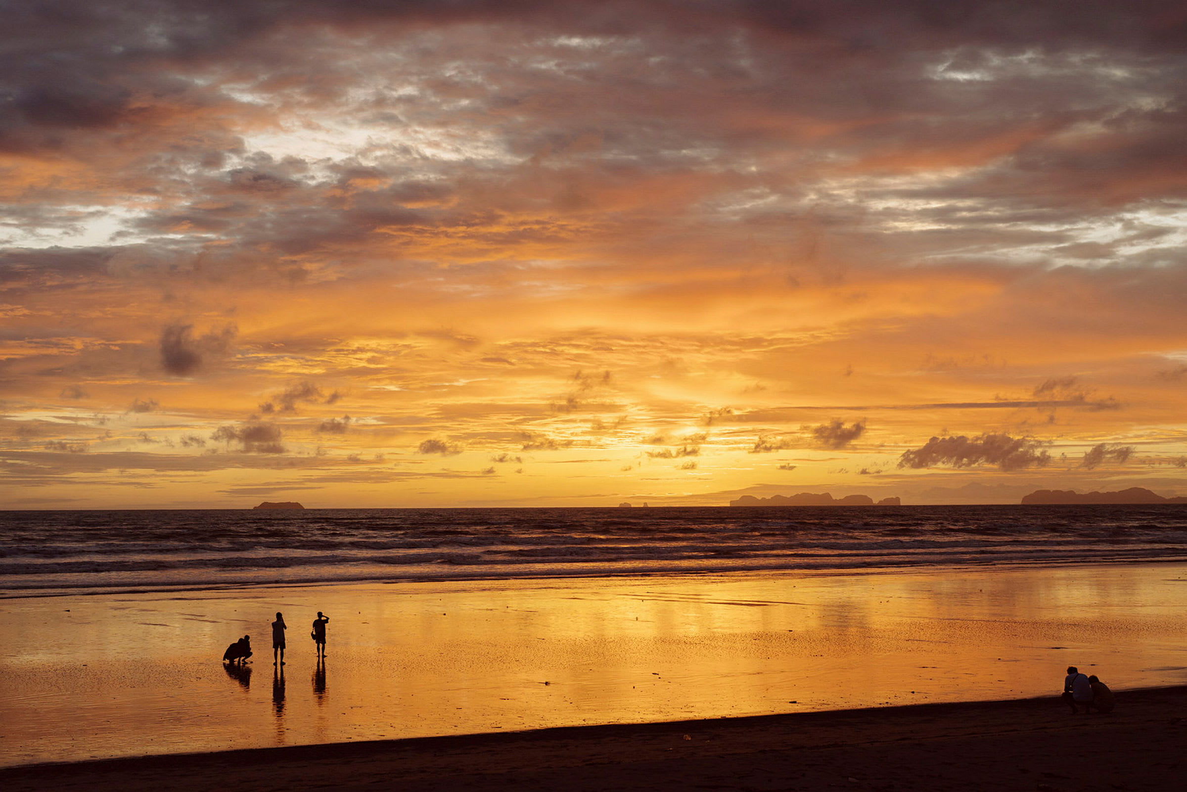 En strand ved solnedgang med noen mennesker som står ved vannet. (AI-generert tekst)