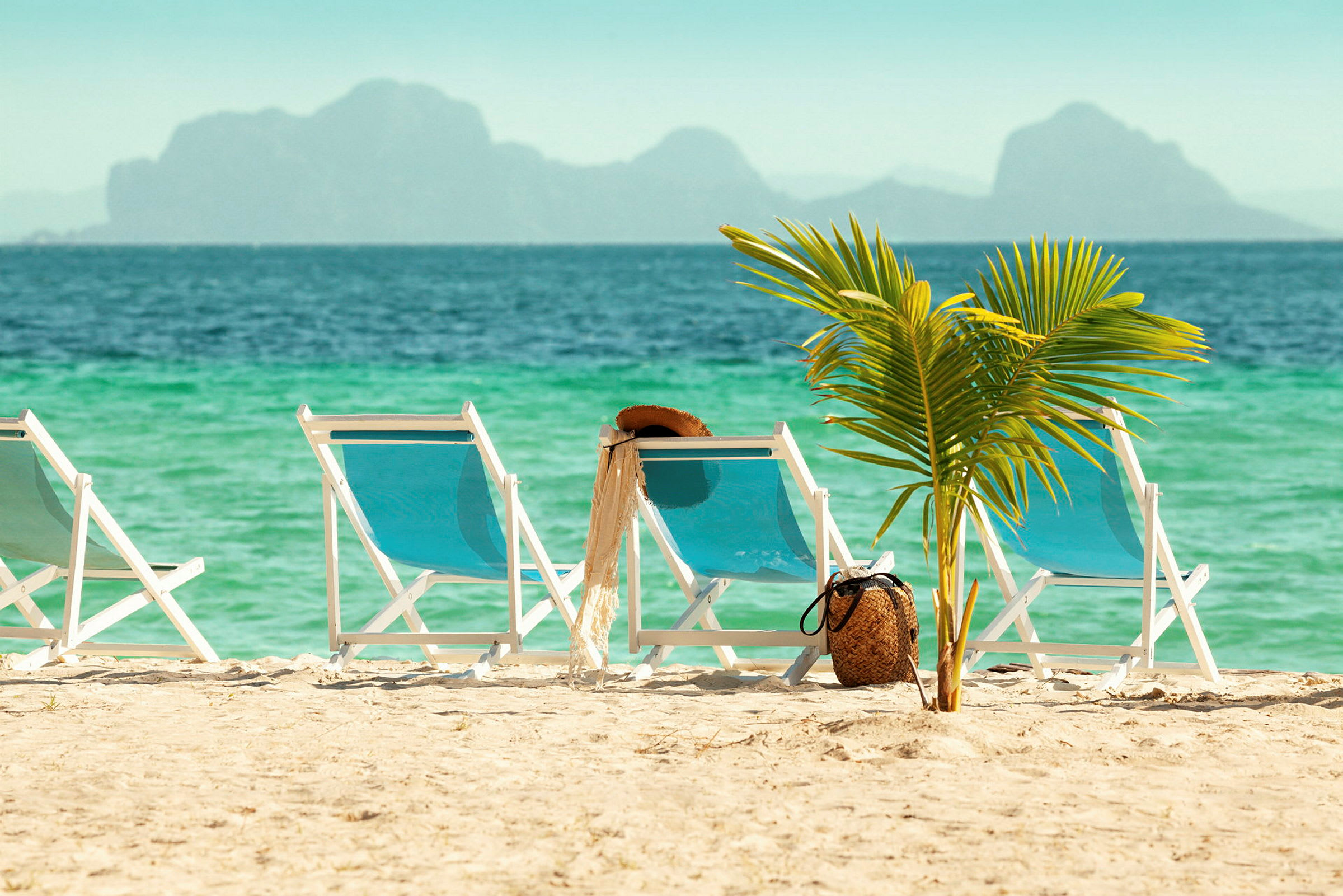 Solstoler på sandstrand med palme og hav i bakgrunnen. (AI-generert tekst)