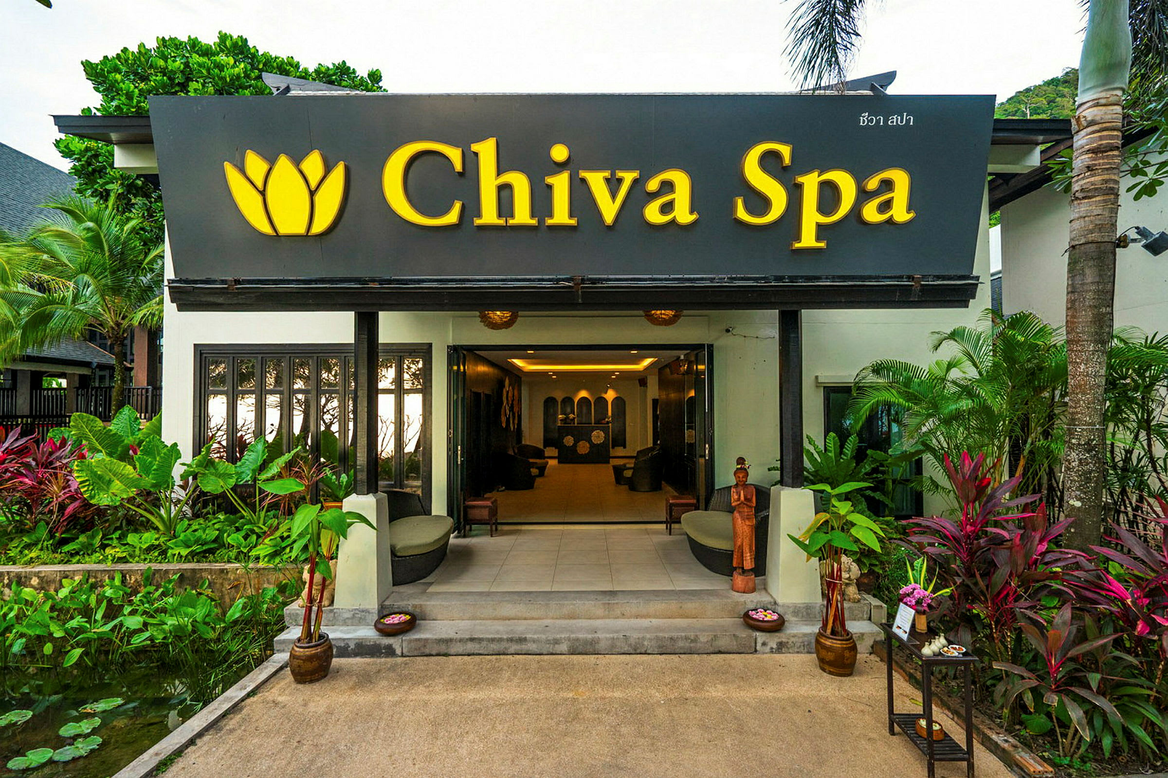 Inngangen til et spa-anlegg med skilt med teksten "Chiva Spa" og omgivende planter. (AI-generert tekst)