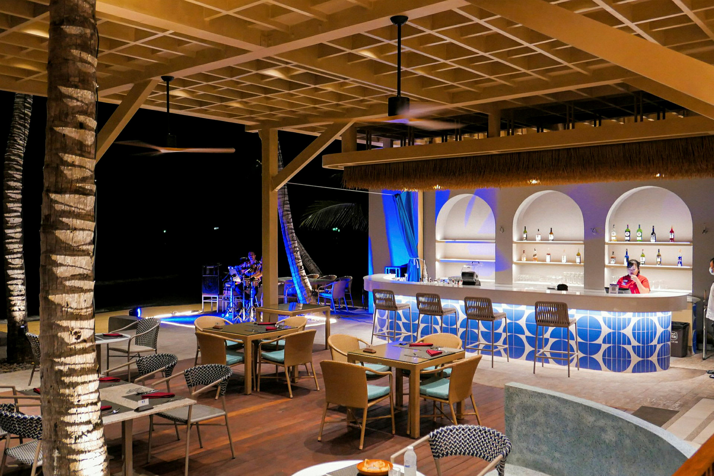 En utendørs bar og restaurant med moderne møbler og en person som spiller musikk i bakgrunnen. (AI-generert tekst)