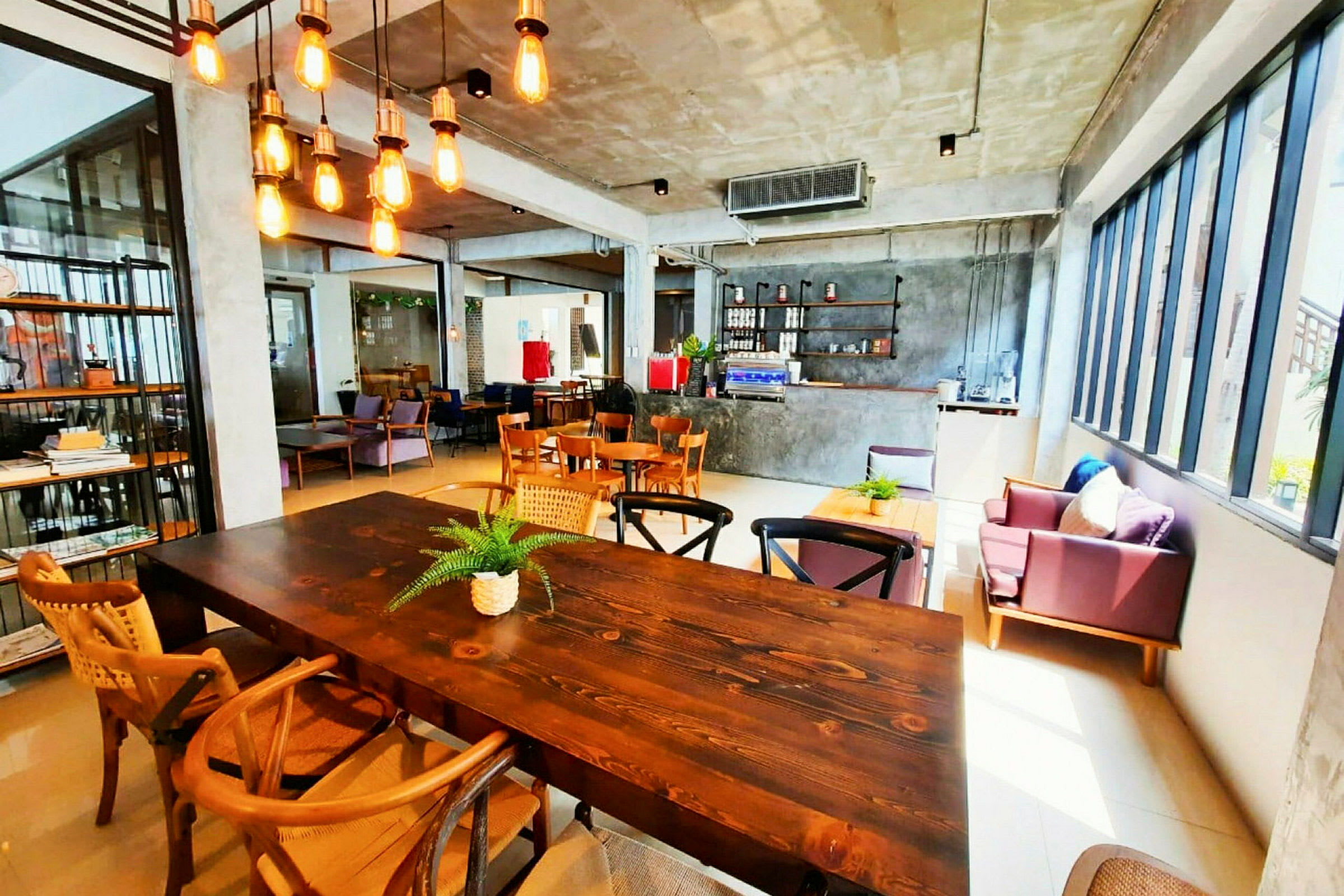 En kafé med lyse industrielle detaljer, trebord og stoler, samt store vinduer som slipper inn mye naturlig lys. (AI-generert tekst)