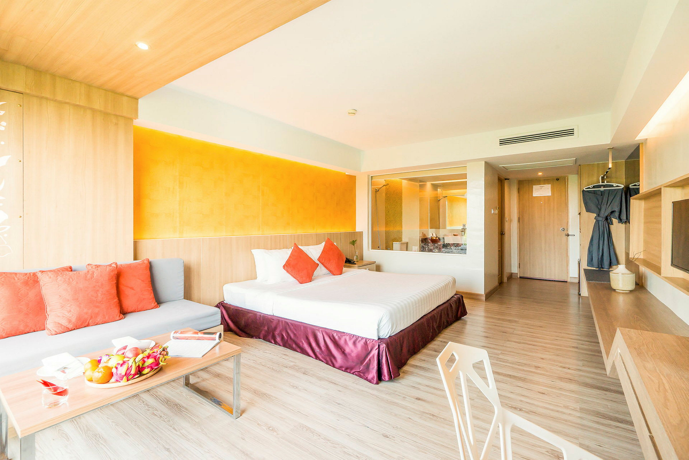 Et moderne hotellrom med dobbeltseng, sofa med puter og et bord med frukt. (AI-generert tekst)