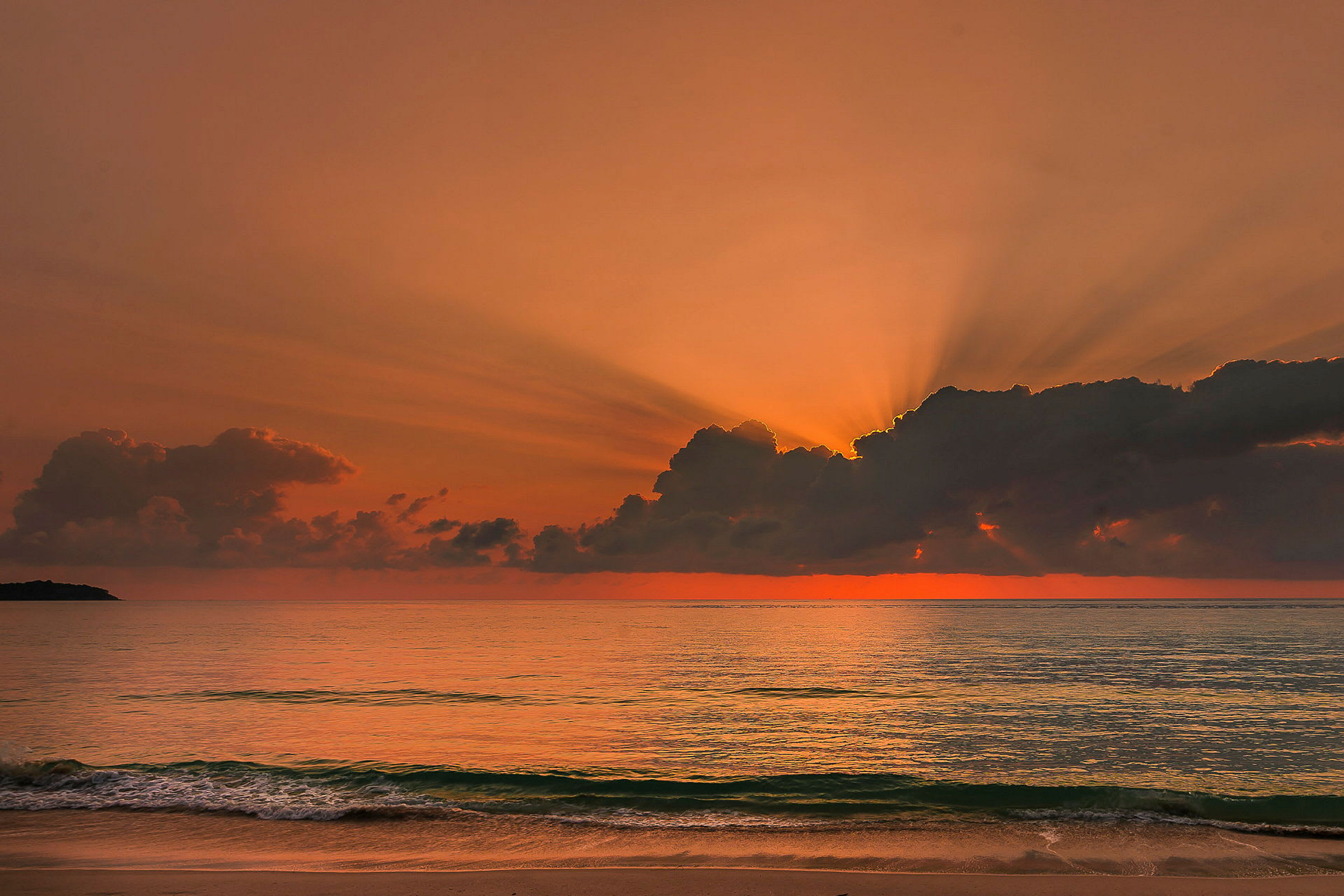 En solnedgang over havet der røde og oransje farger lyser opp skyene, med bølger som ruller inn mot stranden i forgrunnen. (AI-generert tekst)