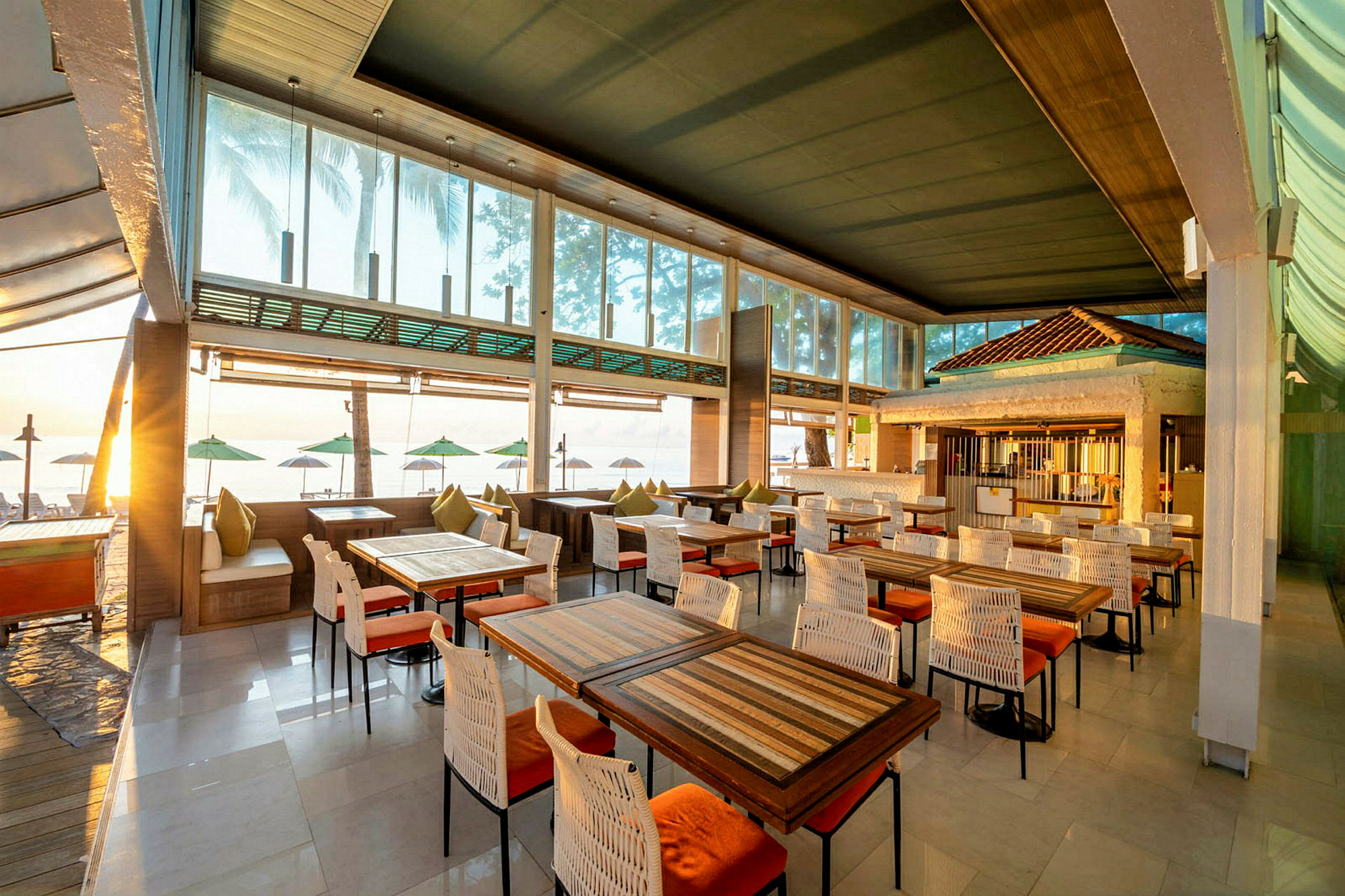 Restaurant med trebord og stoler, med utsikt mot stranden og havet. (AI-generert tekst)