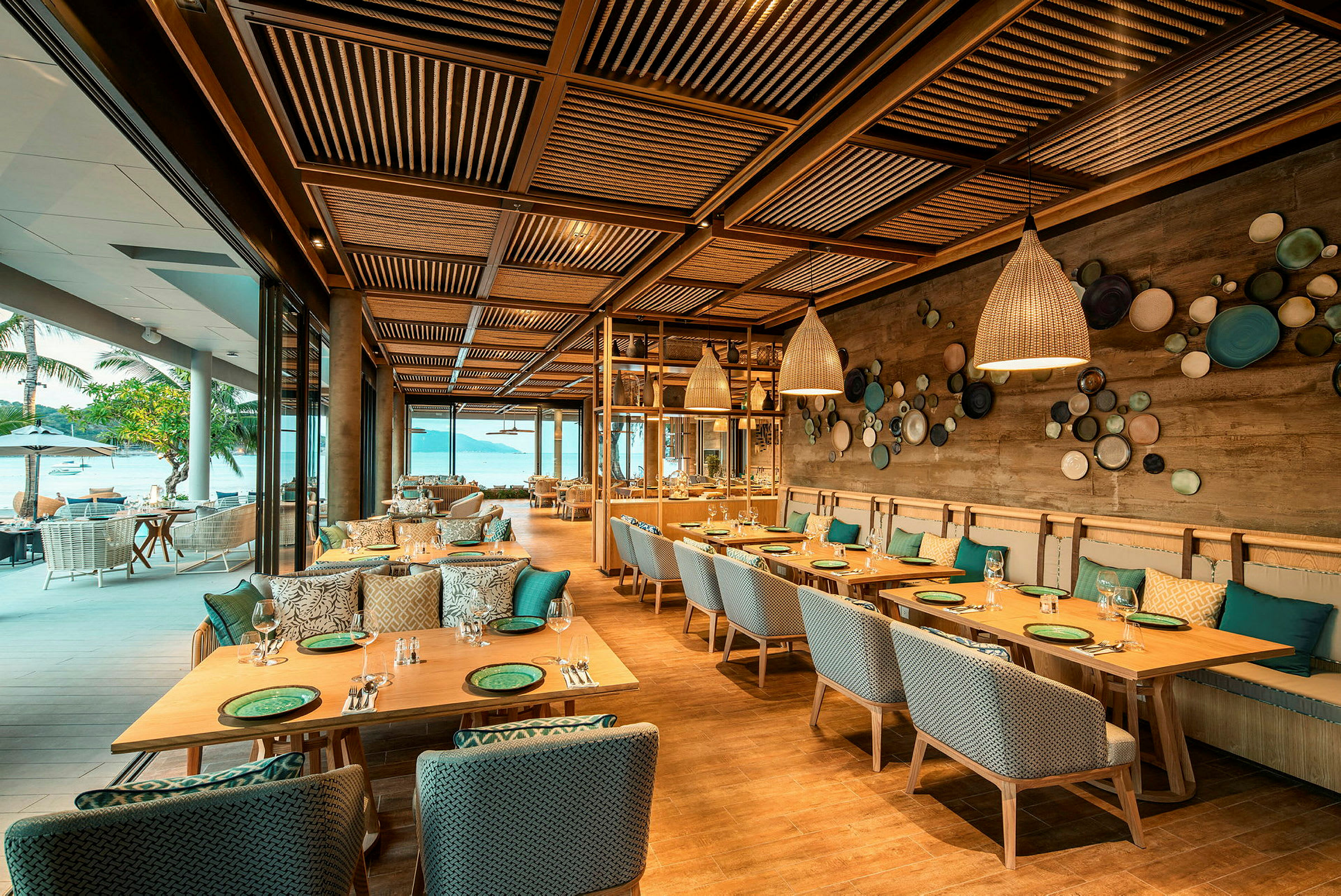 En elegant restaurant med trebord og stoler, dekorert med moderne lamper og kunst på veggene, med utsikt mot havet. (AI-generert tekst)