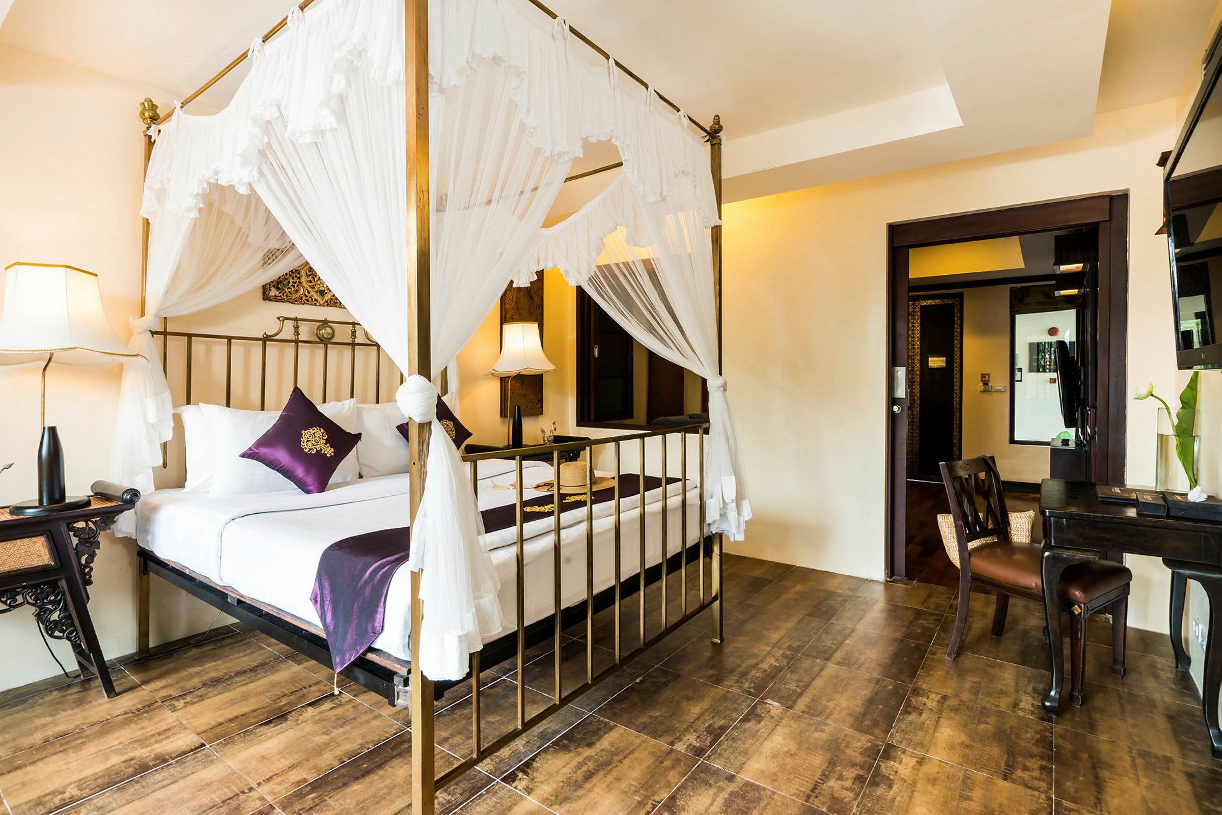 Et hotellrom med en seng med himmelseng og hvite gardiner, omgitt av elegante møbler og myk belysning. (AI-generert tekst)