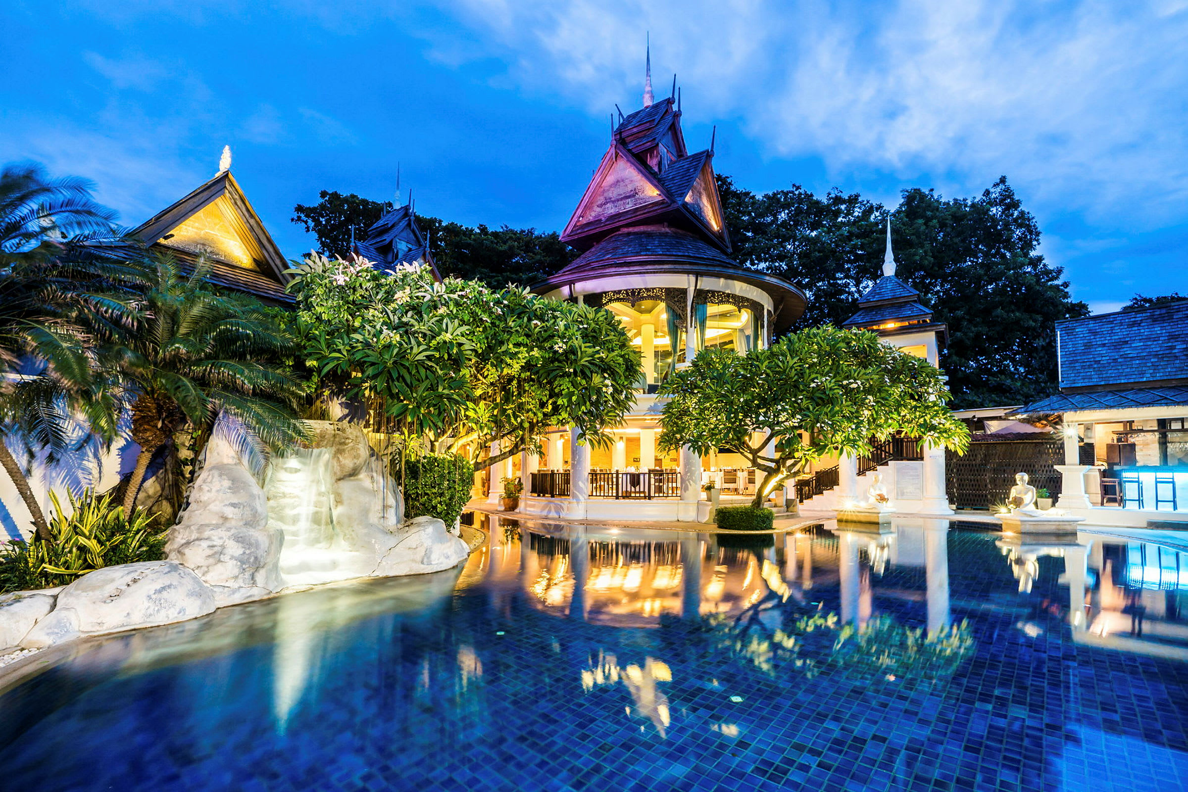 Et opplyst hotell med thailandsk arkitektur og basseng i forgrunnen under skumringen. (AI-generert tekst)