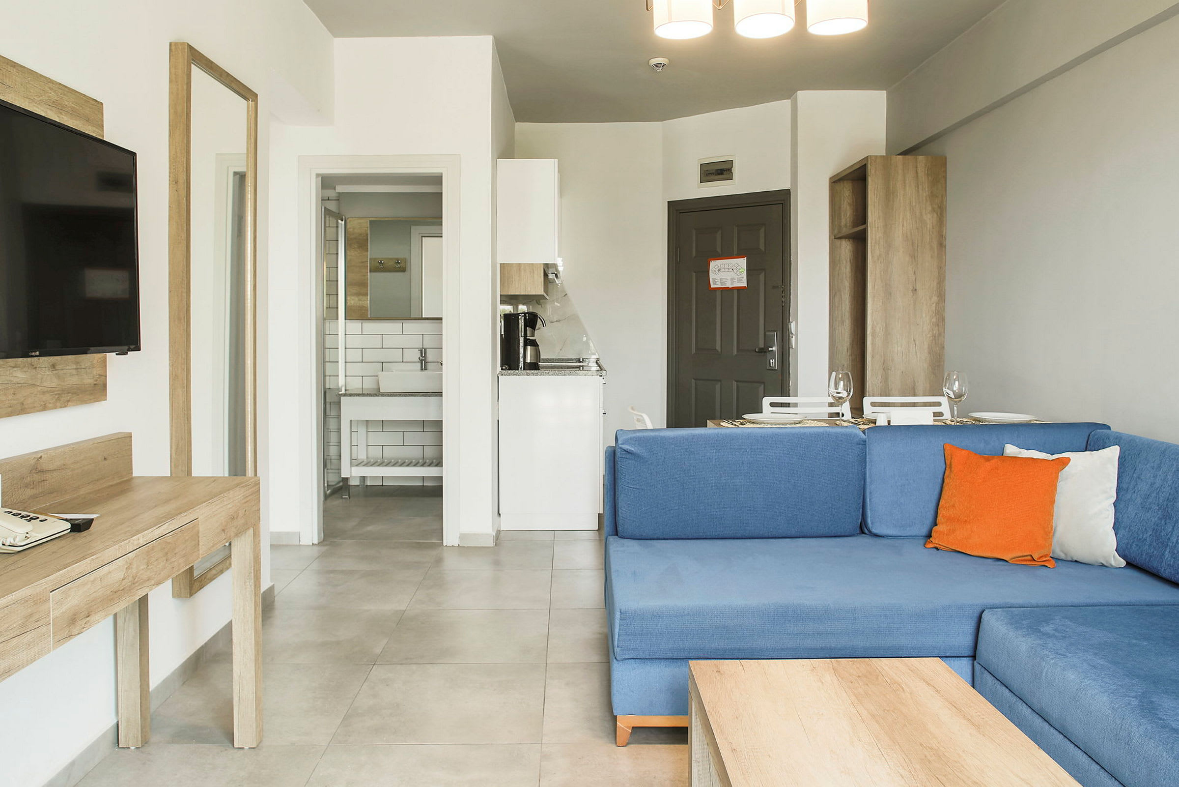 Et hotellrom med blå sofa, skrivebord, TV, kjøkken og bad. (AI-generert tekst)