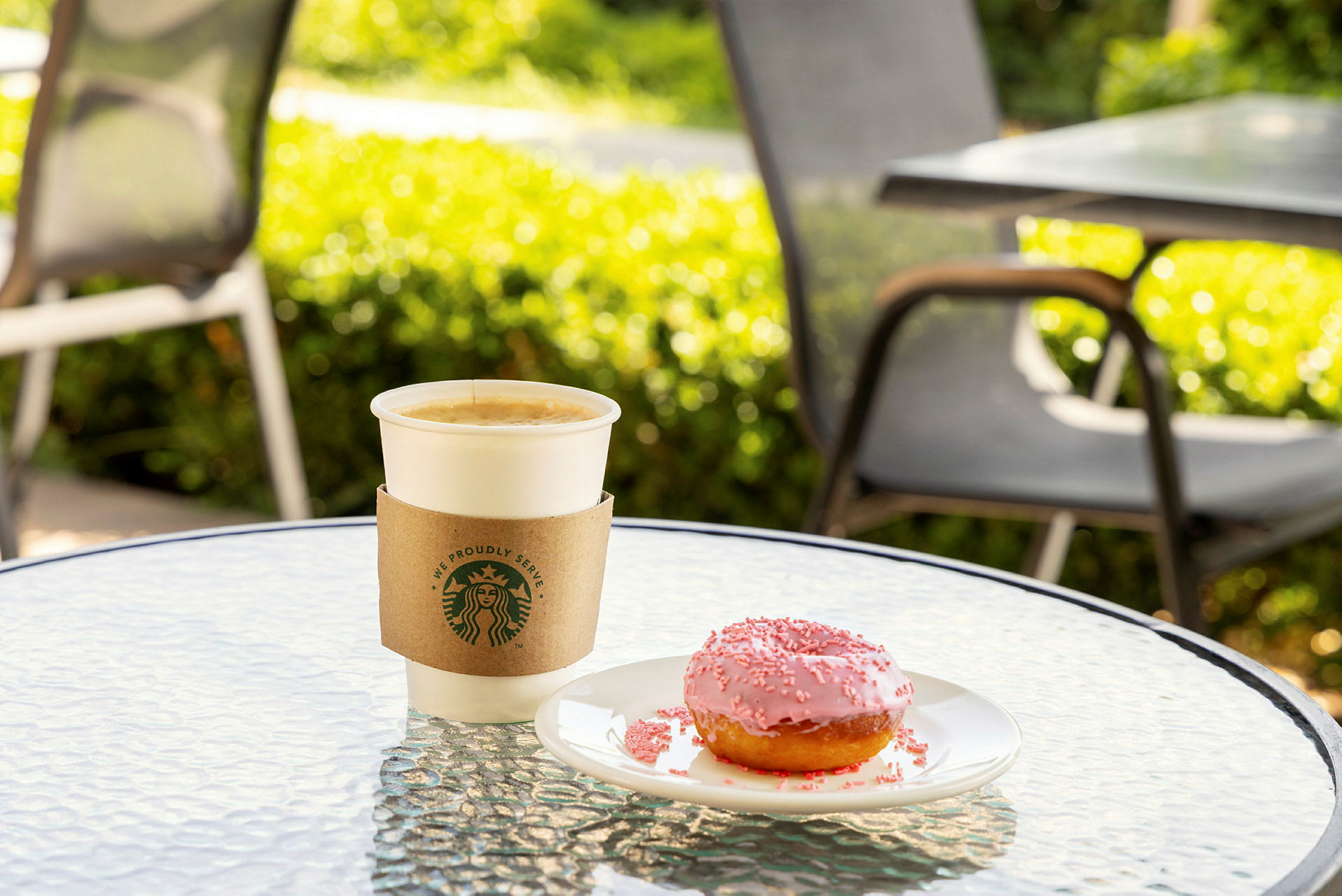 En kopp kaffe og en rosa smultring på et bord utendørs. (AI-generert tekst)