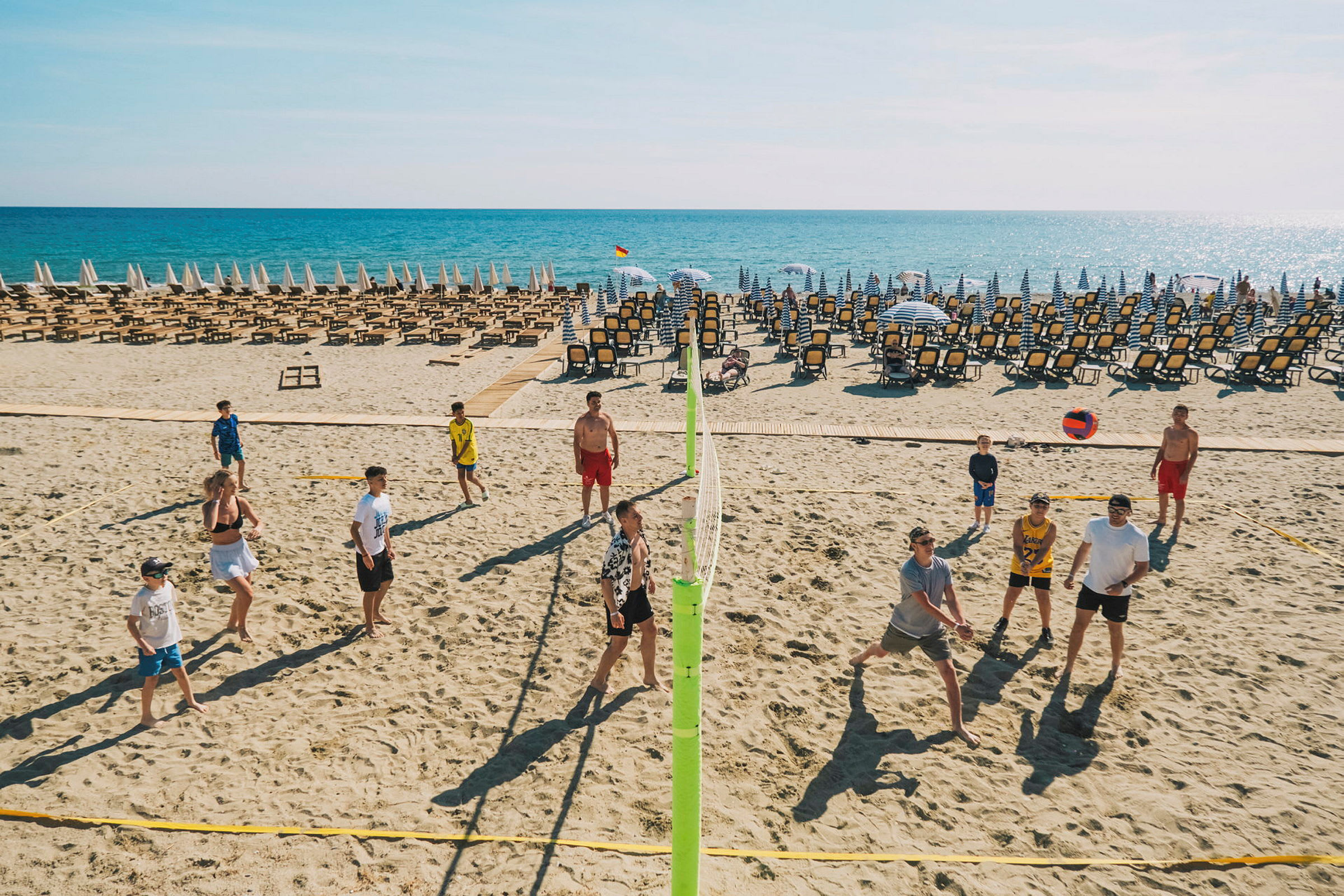 En strand med solsenger og parasoller, folk spiller volleyball. (AI-generert tekst)