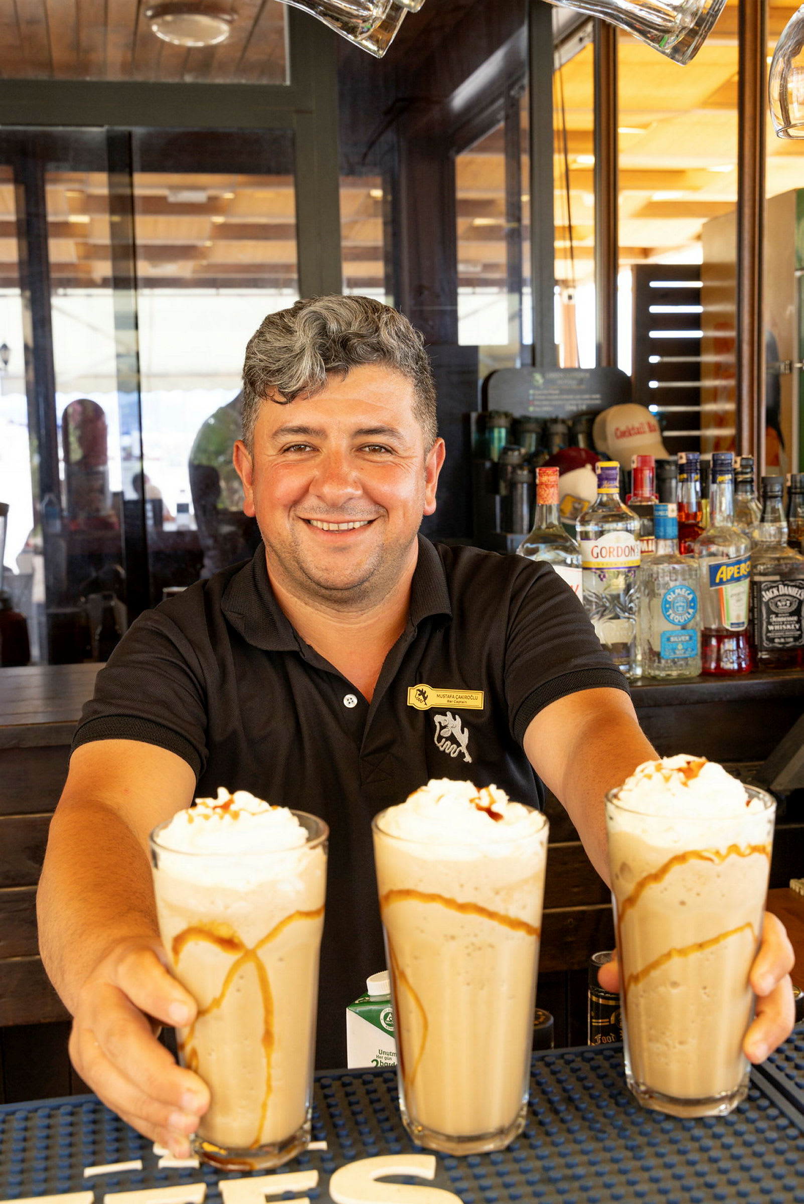 En bartender holder tre glass med milkshakes toppet med krem og karamellsaus. (AI-generert tekst)
