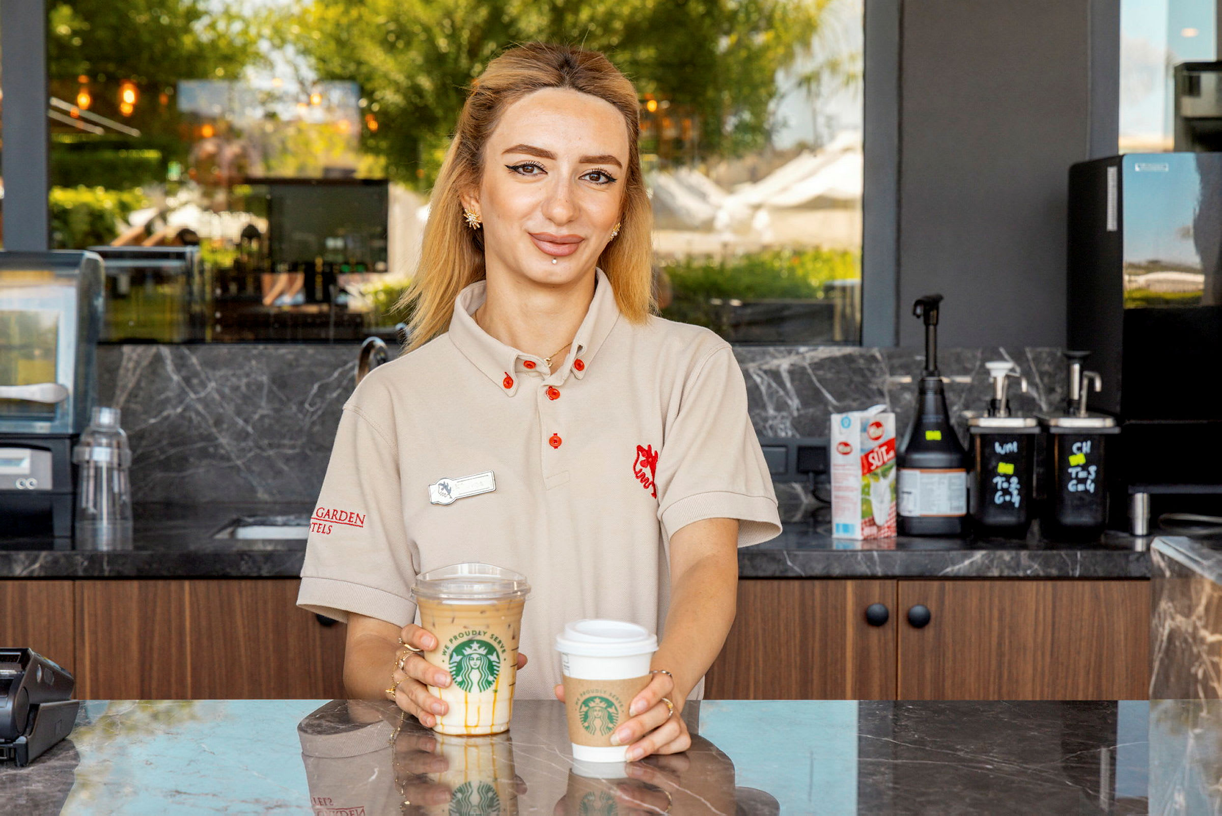En kvinne står bak en disk og holder to kaffekopper fra Starbucks i hendene. (AI-generert tekst)