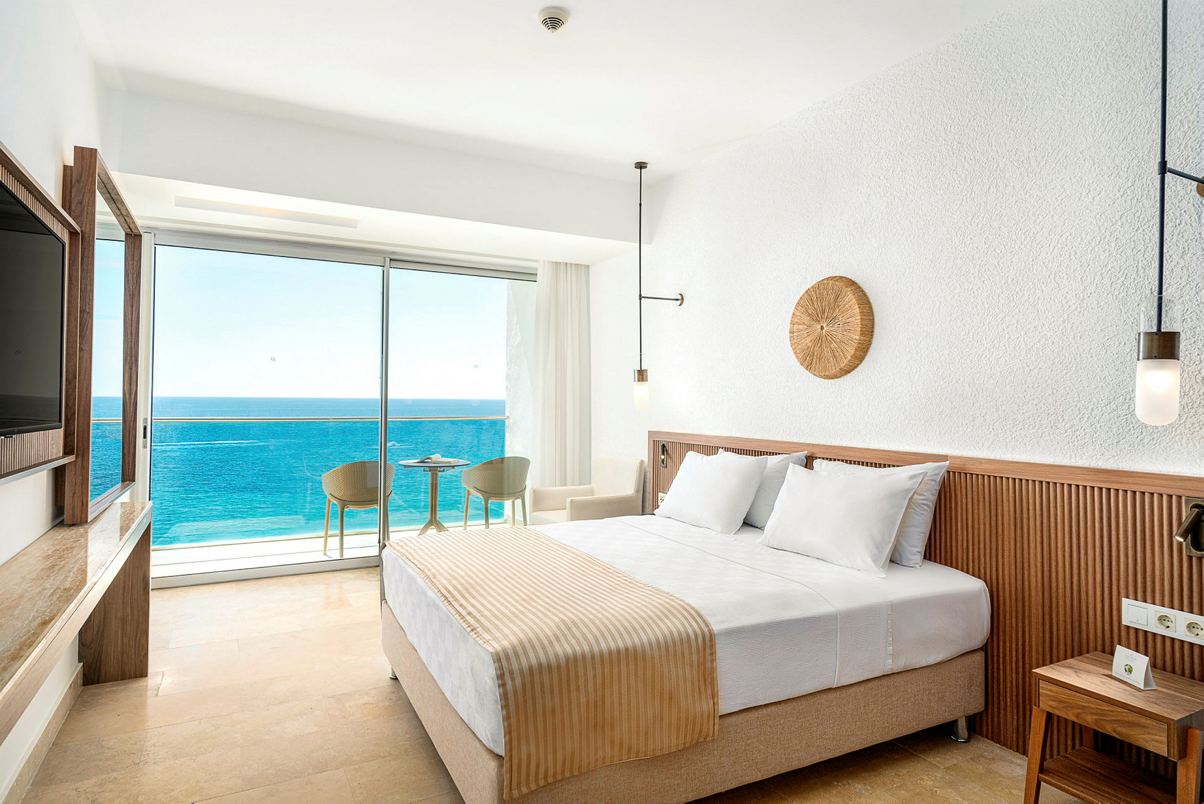 Hotellrom med en dobbeltseng og balkong med utsikt over havet. (AI-generert tekst)