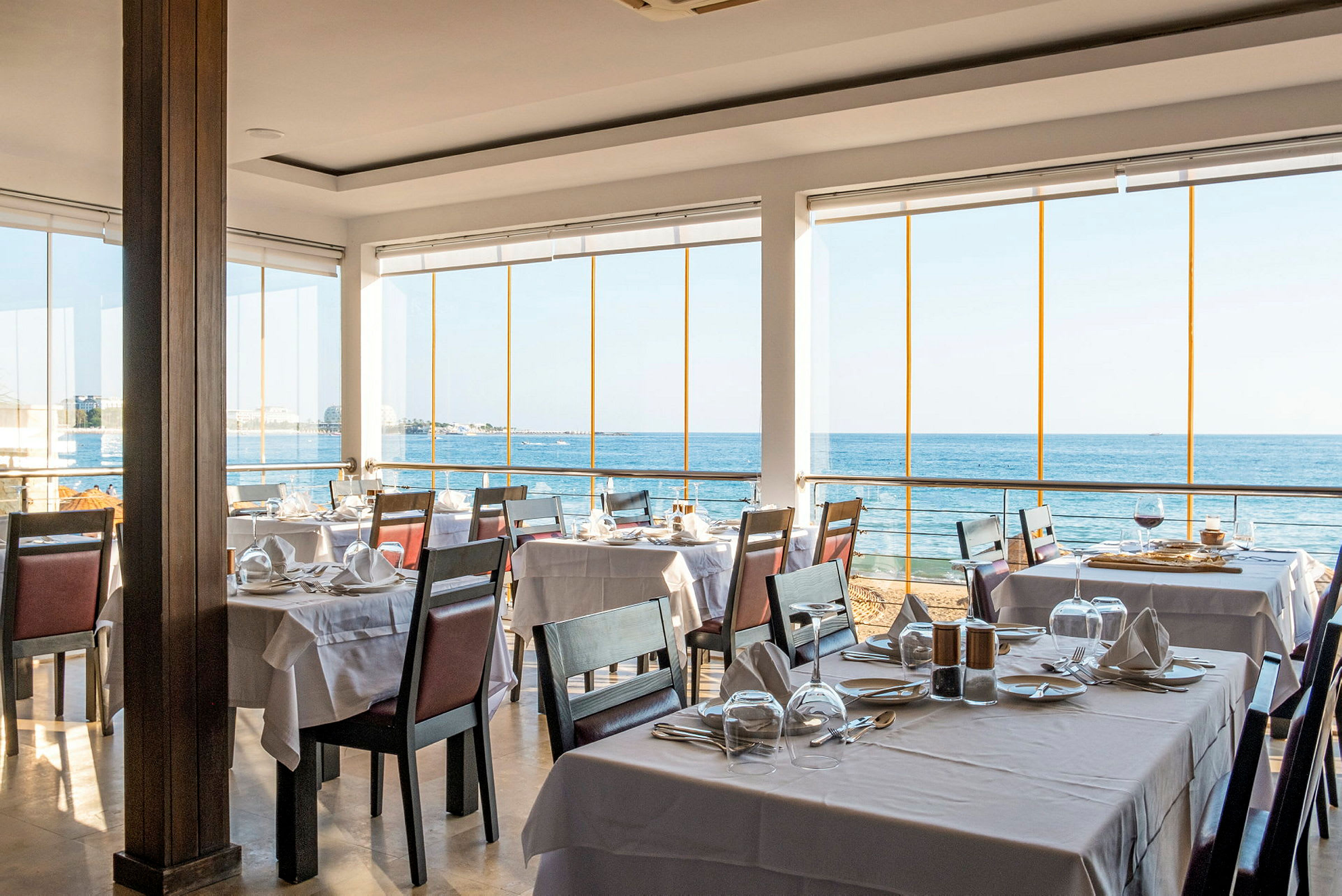 Restaurant med dekkede bord og utsikt over havet. (AI-generert tekst)