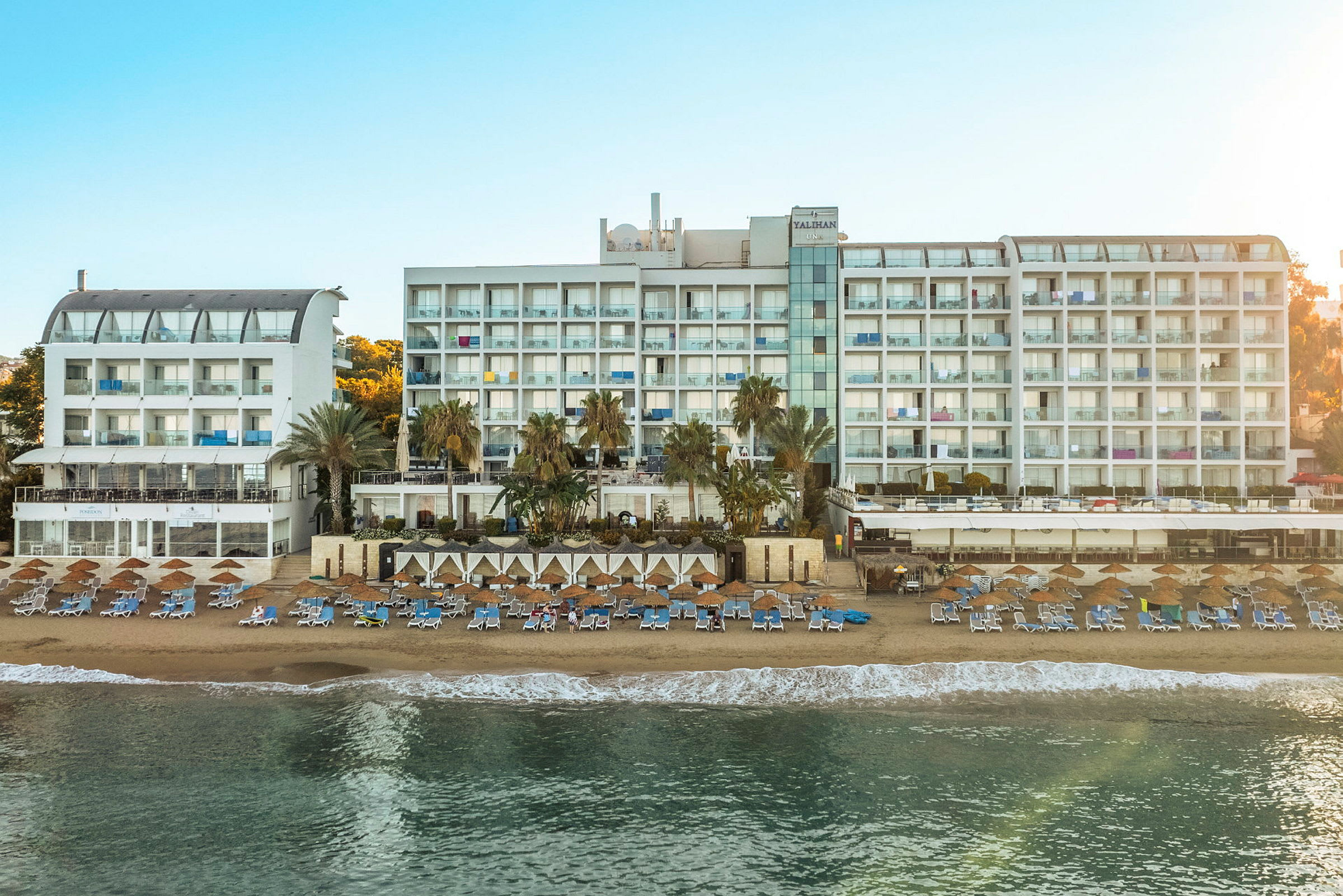 Bilde av en stor hvit hotellbygning ved en solrik strand med solsenger og parasoller. (AI-generert tekst)