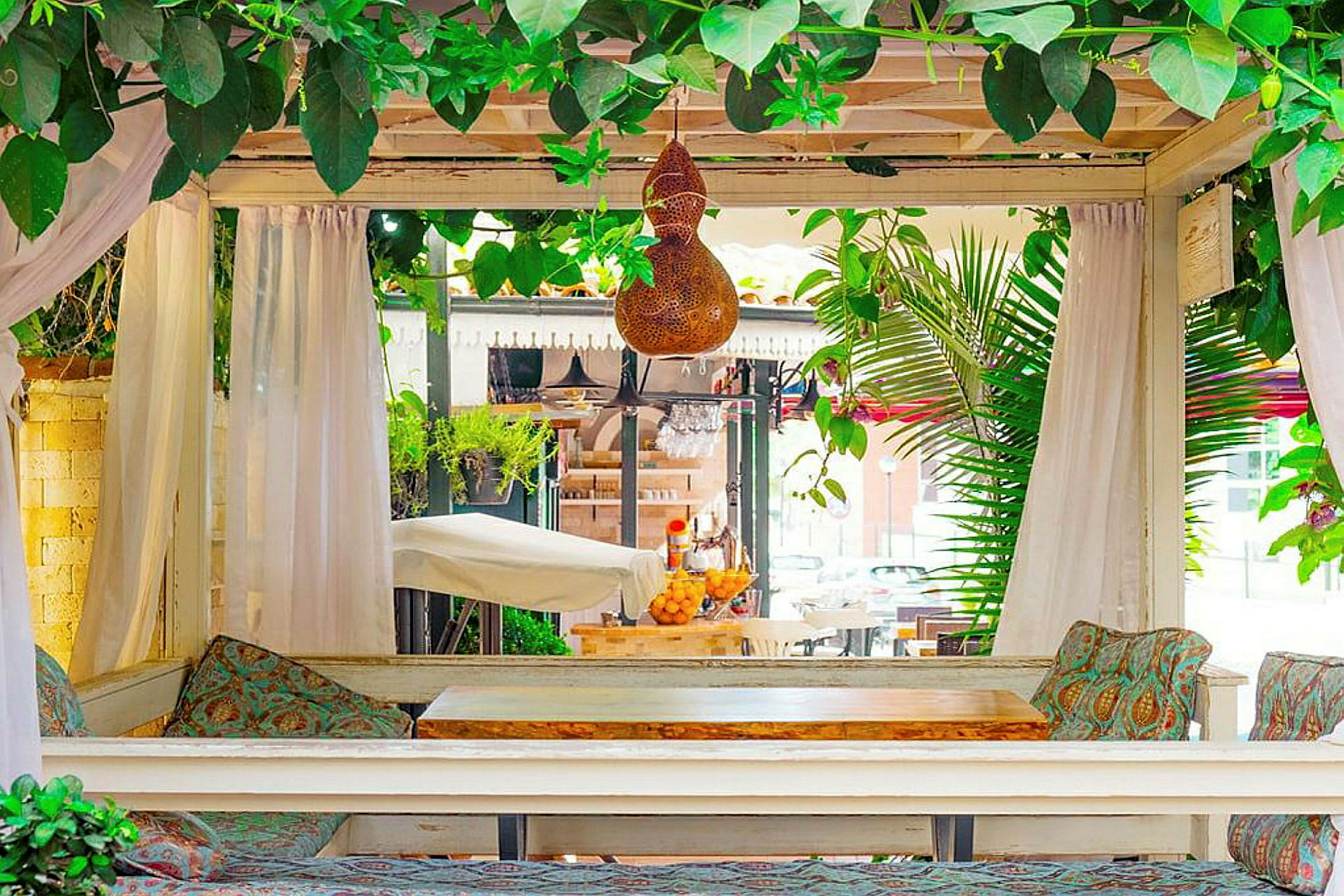 En terrasse med bord og stoler, omgitt av grønne planter og gardiner. (AI-generert tekst)