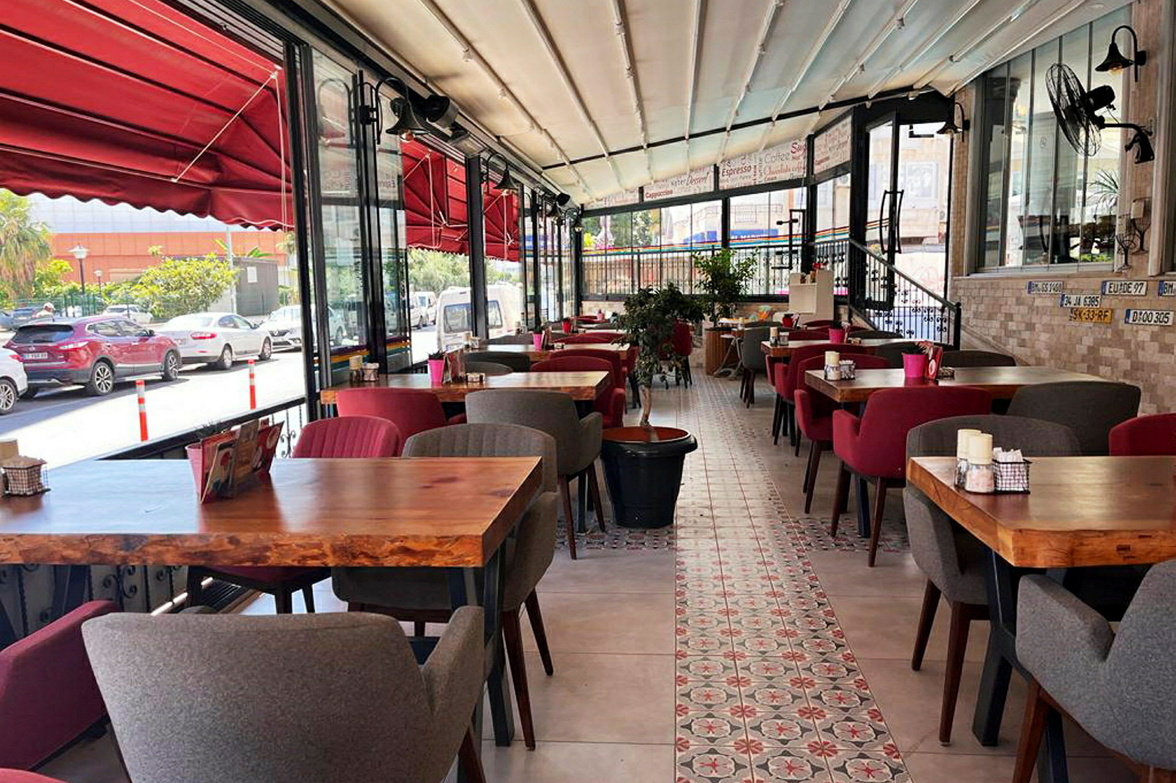 Bilde av en restaurant med rødt interiør, trebord og polstrede stoler. Utsikt over gaten sees gjennom glassvinduer. (AI-generert tekst)