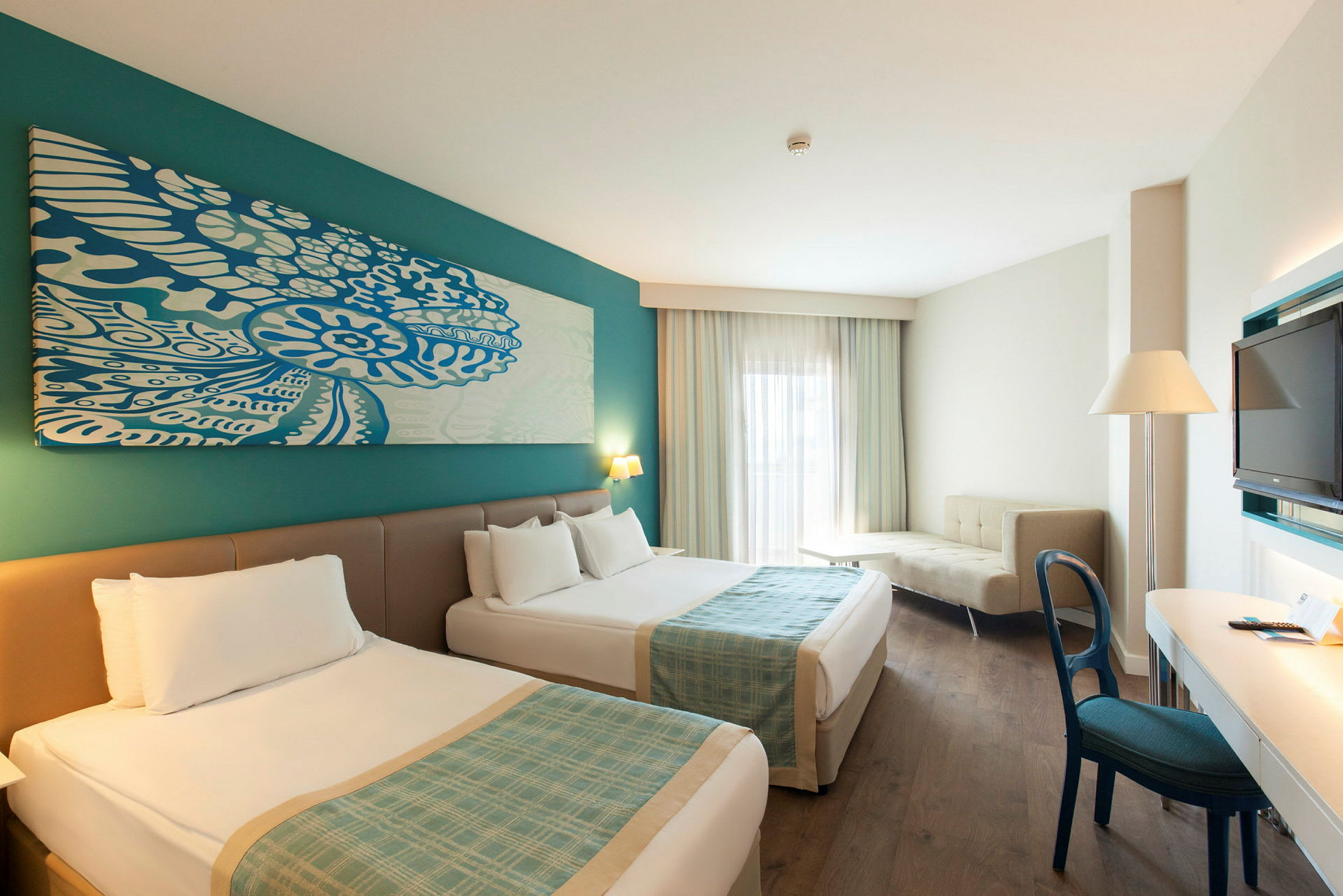 Hotellrom med to senger, skrivebord, sofa og TV. (AI-generert tekst)