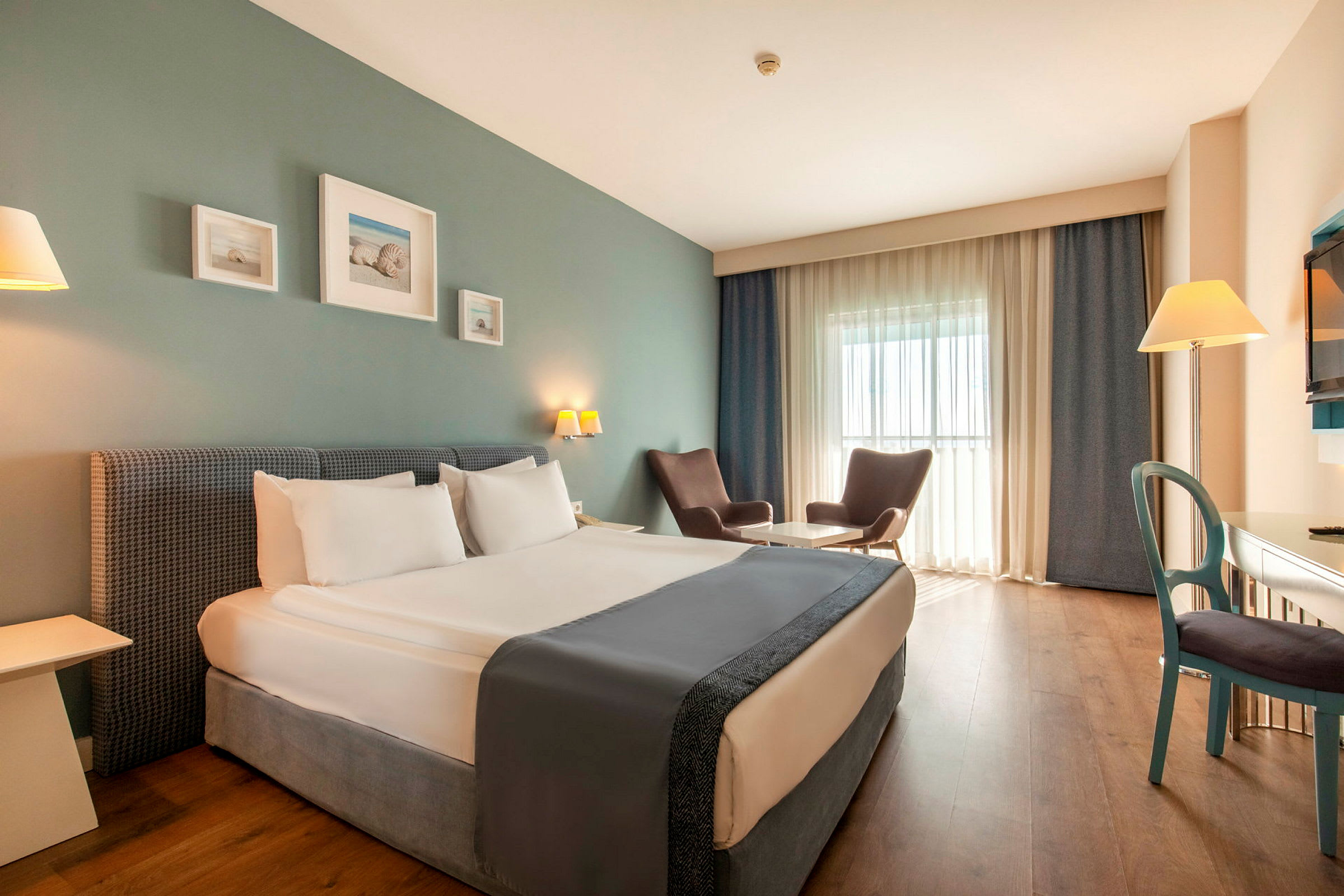 Et hotellrom med en dobbeltseng, to lenestoler ved et bord, et skrivebord og en TV. (AI-generert tekst)