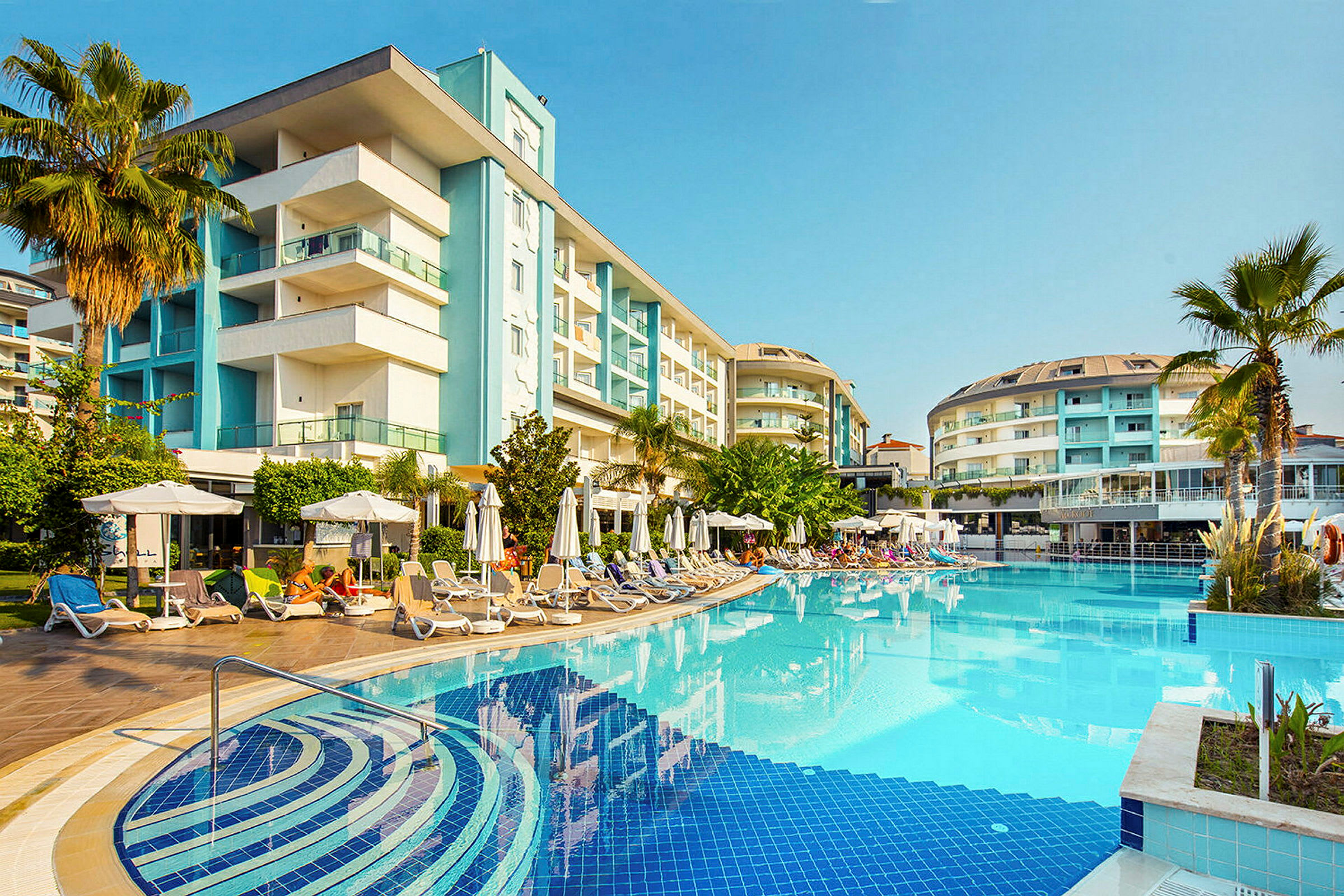 Hotell bygget rundt et utendørs basseng med solsenger og parasoller. (AI-generert tekst)