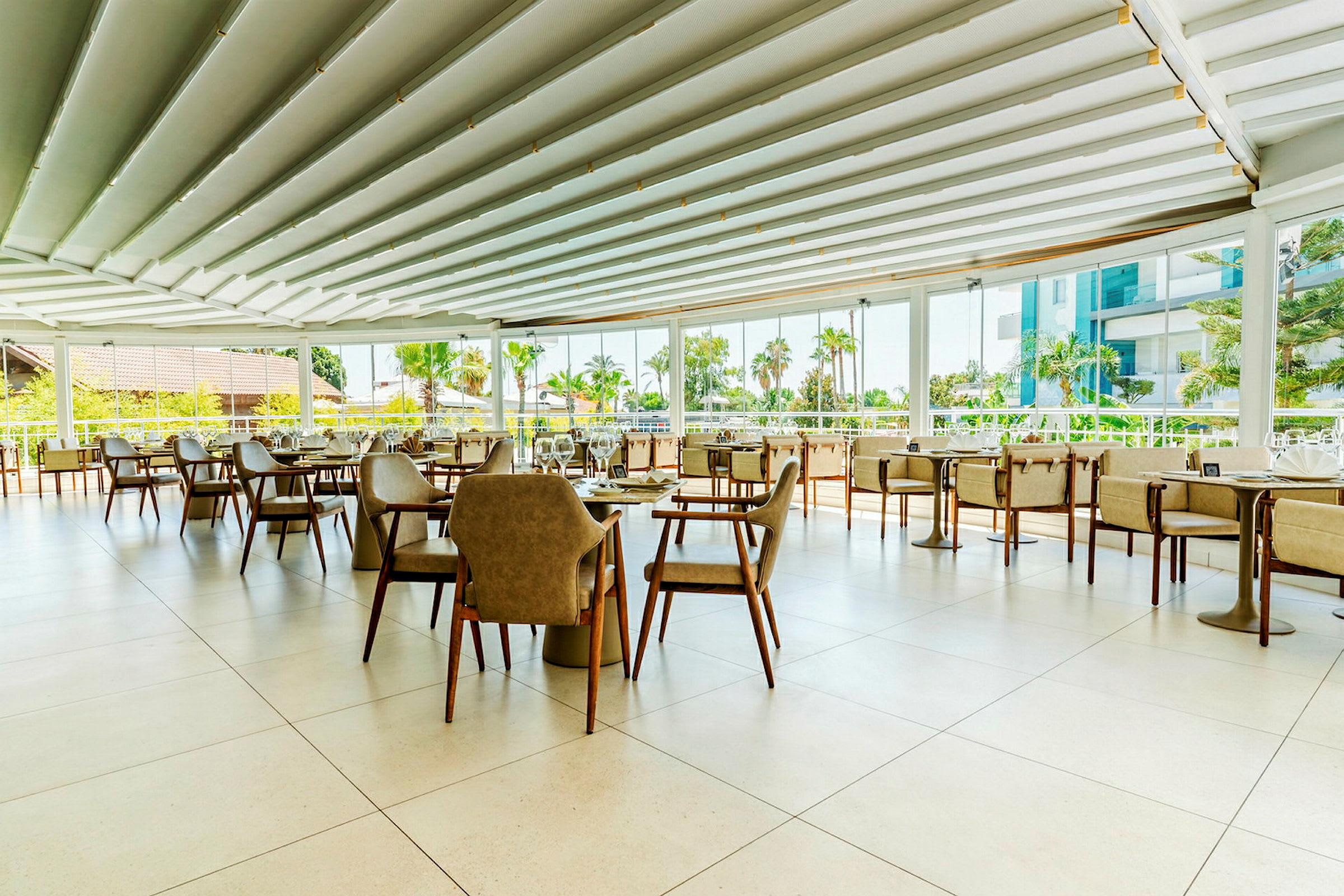 Lyse og moderne møbler i en restaurant med åpen takløsning og panoramavinduer som vender ut mot en grønn utsikt. (AI-generert tekst)