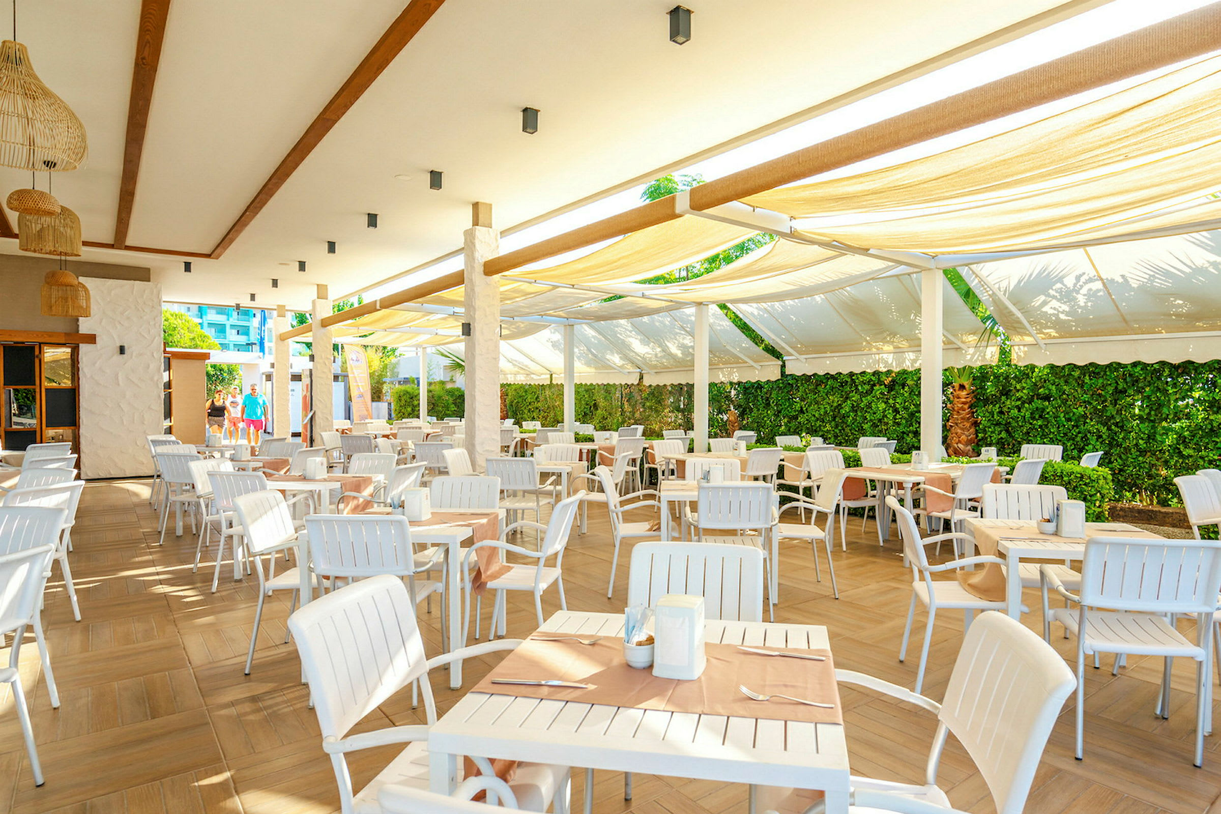 Utendørs serveringsområde med hvite bord og stoler under en overbygget terrasse. (AI-generert tekst)
