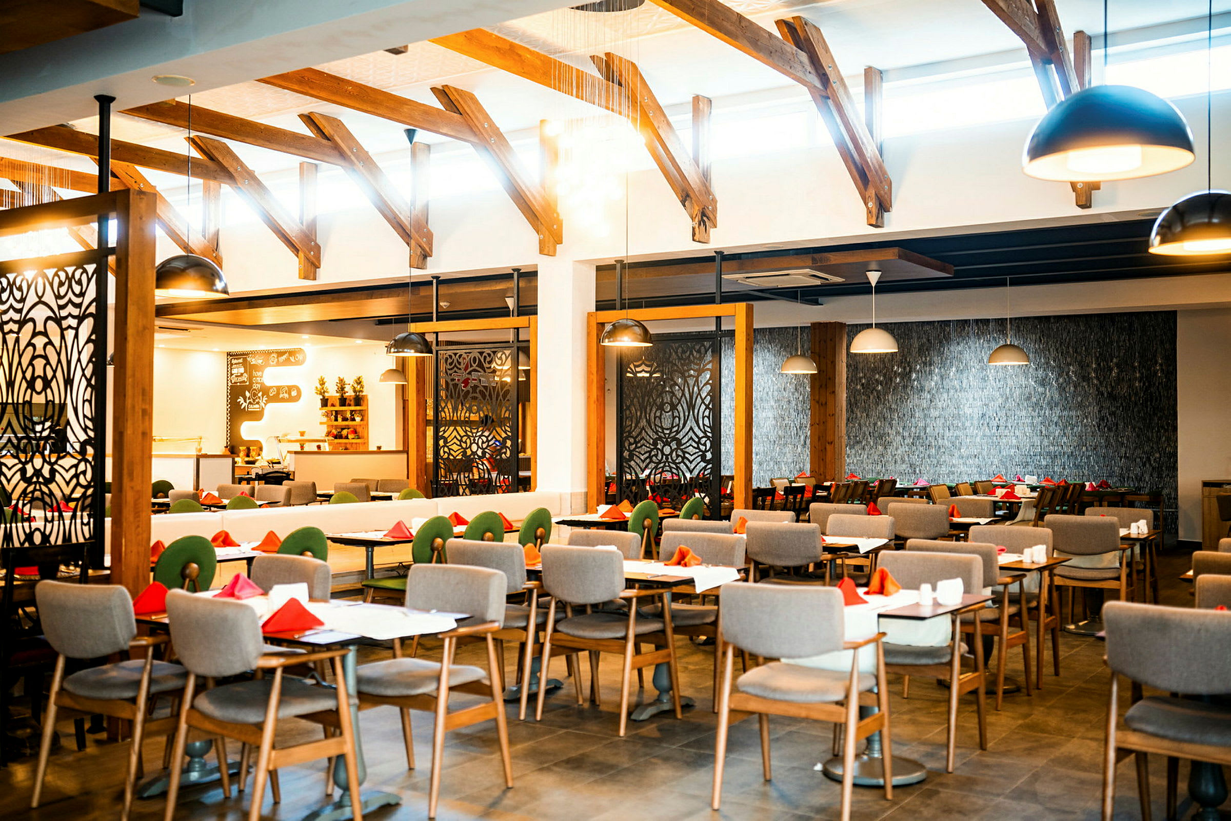 Interiøret i en restaurant med oppstilte dekkede bord og stoler, med takbjelker og moderne designede lamper. (AI-generert tekst)