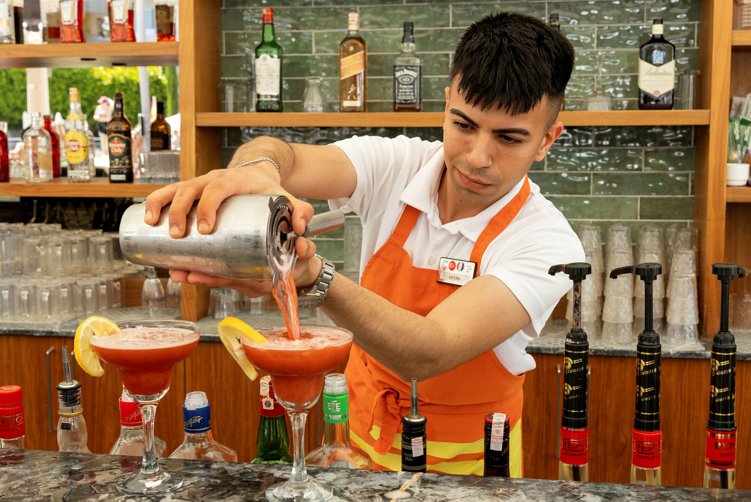 En bartender heller en rød drikk i cocktailglass. (AI-generert tekst)