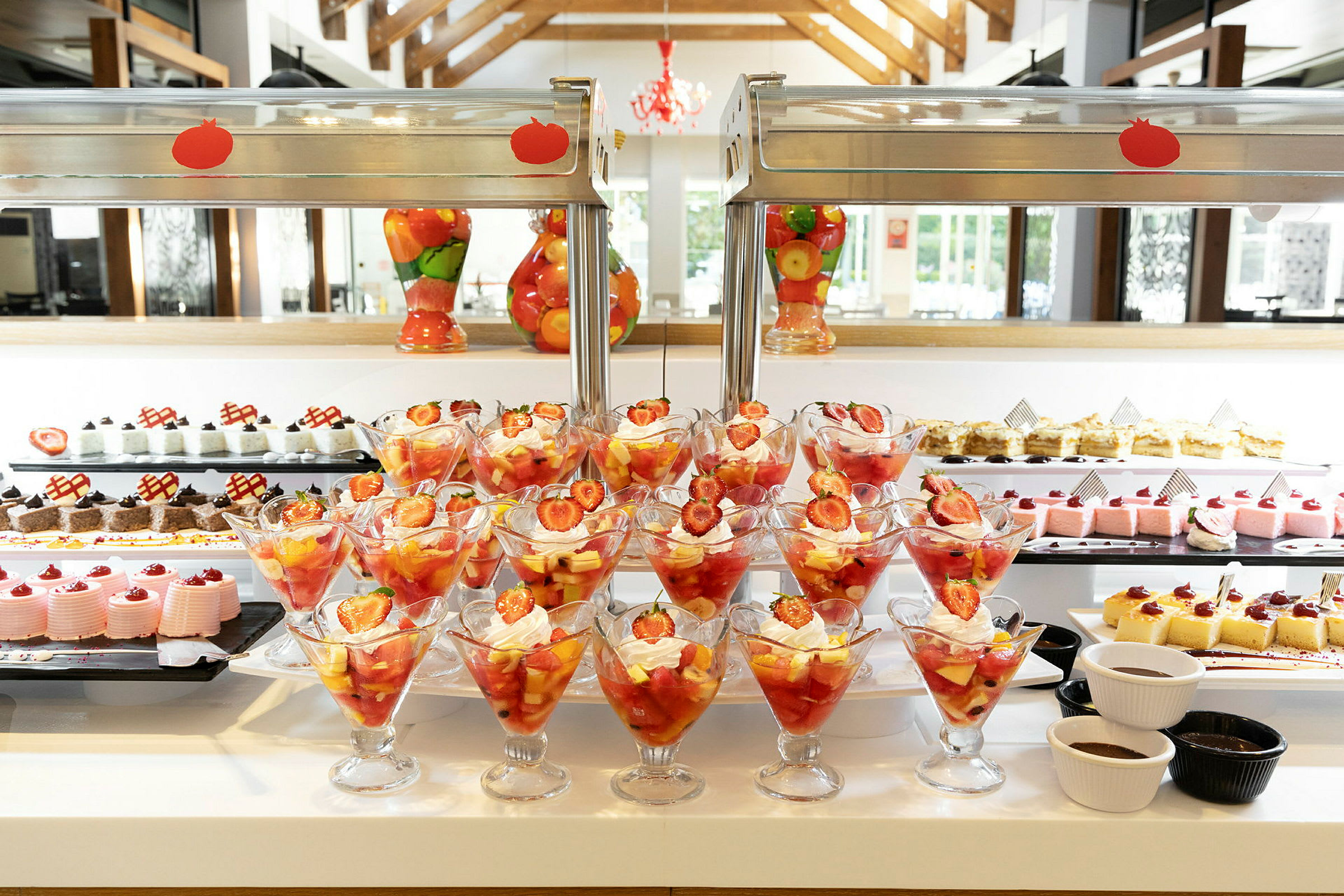 Fruktcocktail med jordbær og pisket krem i glass foran en dessertbuffé. (AI-generert tekst)