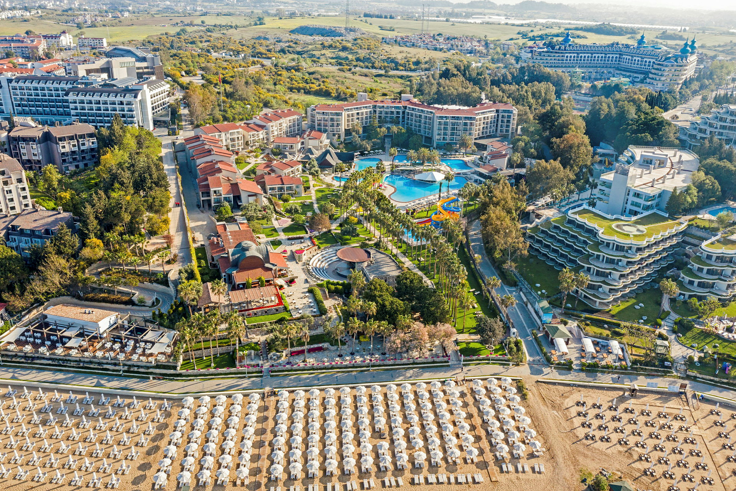 Hotellkompleks med basseng, hager og strand med solsenger og parasoller. (AI-generert tekst)