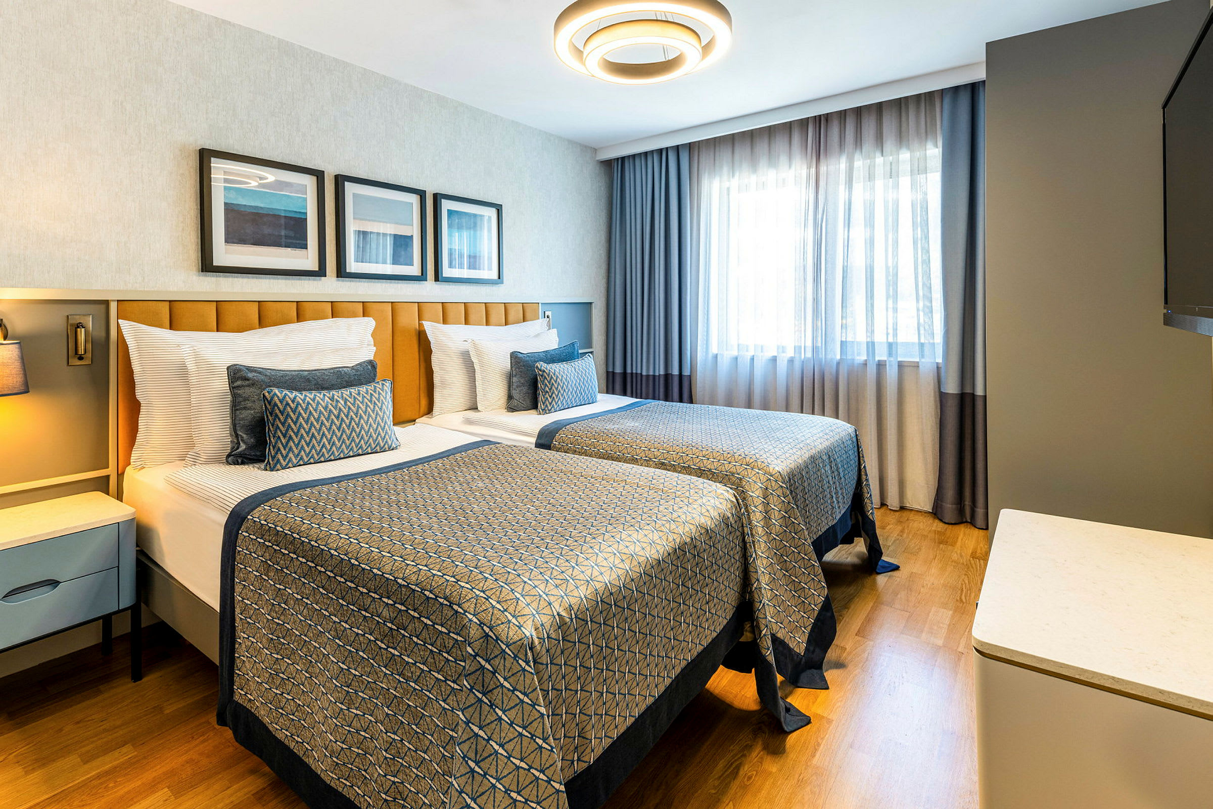 Et hotellrom med to enkeltsenger, moderne innredning og naturlig lys fra et vindu. (AI-generert tekst)