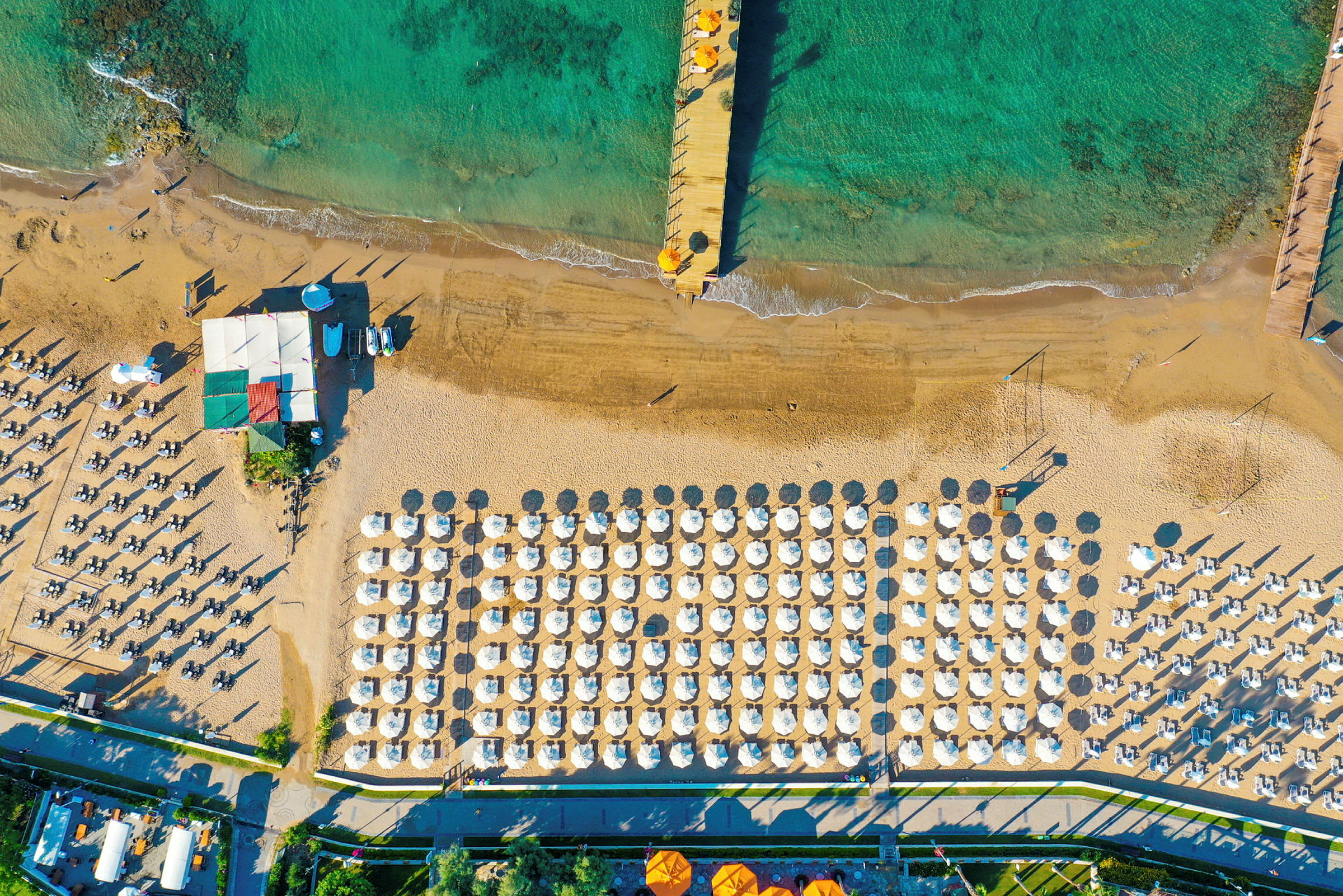 Flyfoto av en strand med parasoller og solsenger. (AI-generert tekst)