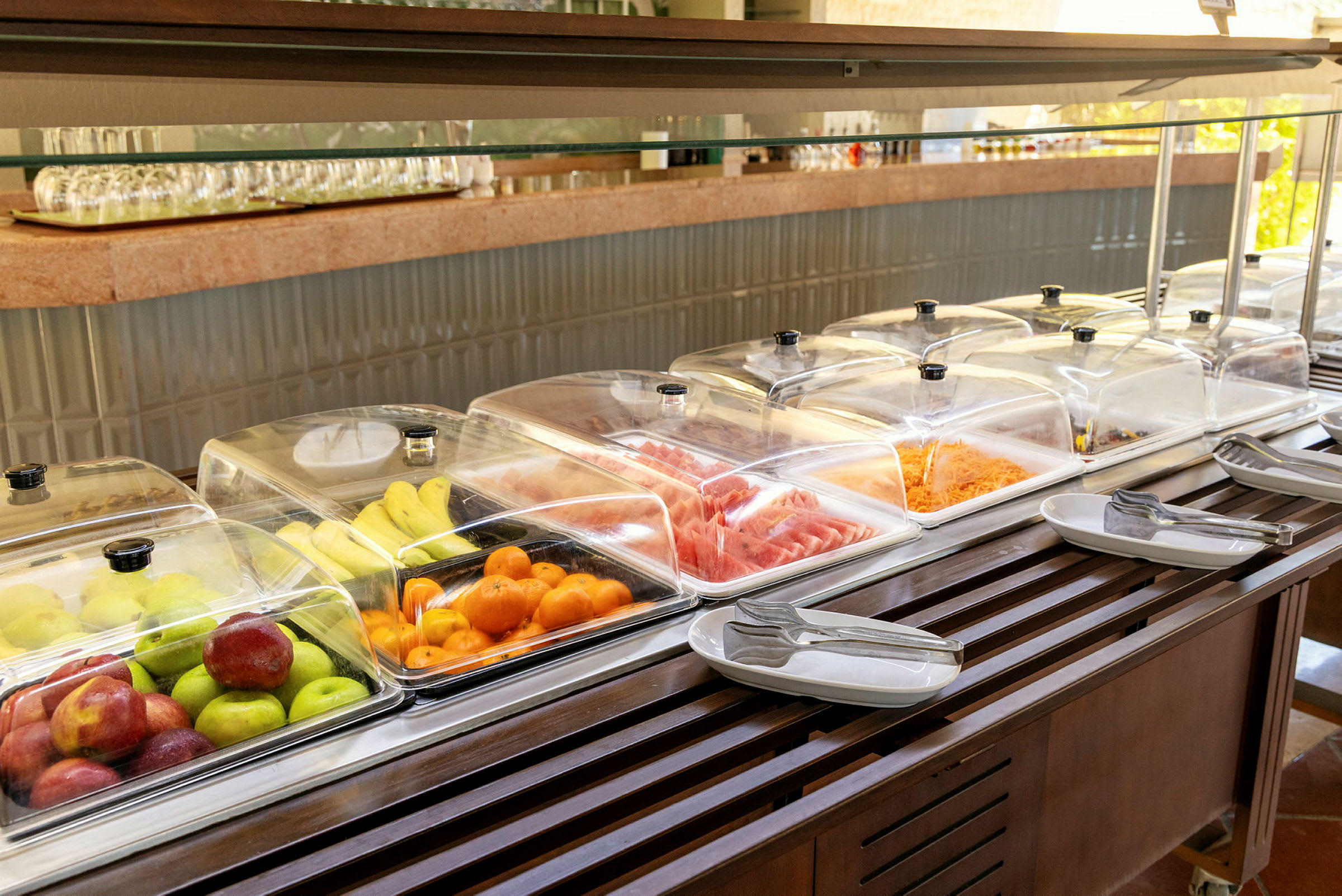 Buffébord med frukt, grønnsaker og kalde retter under gjennomsiktige lokk. (AI-generert tekst)