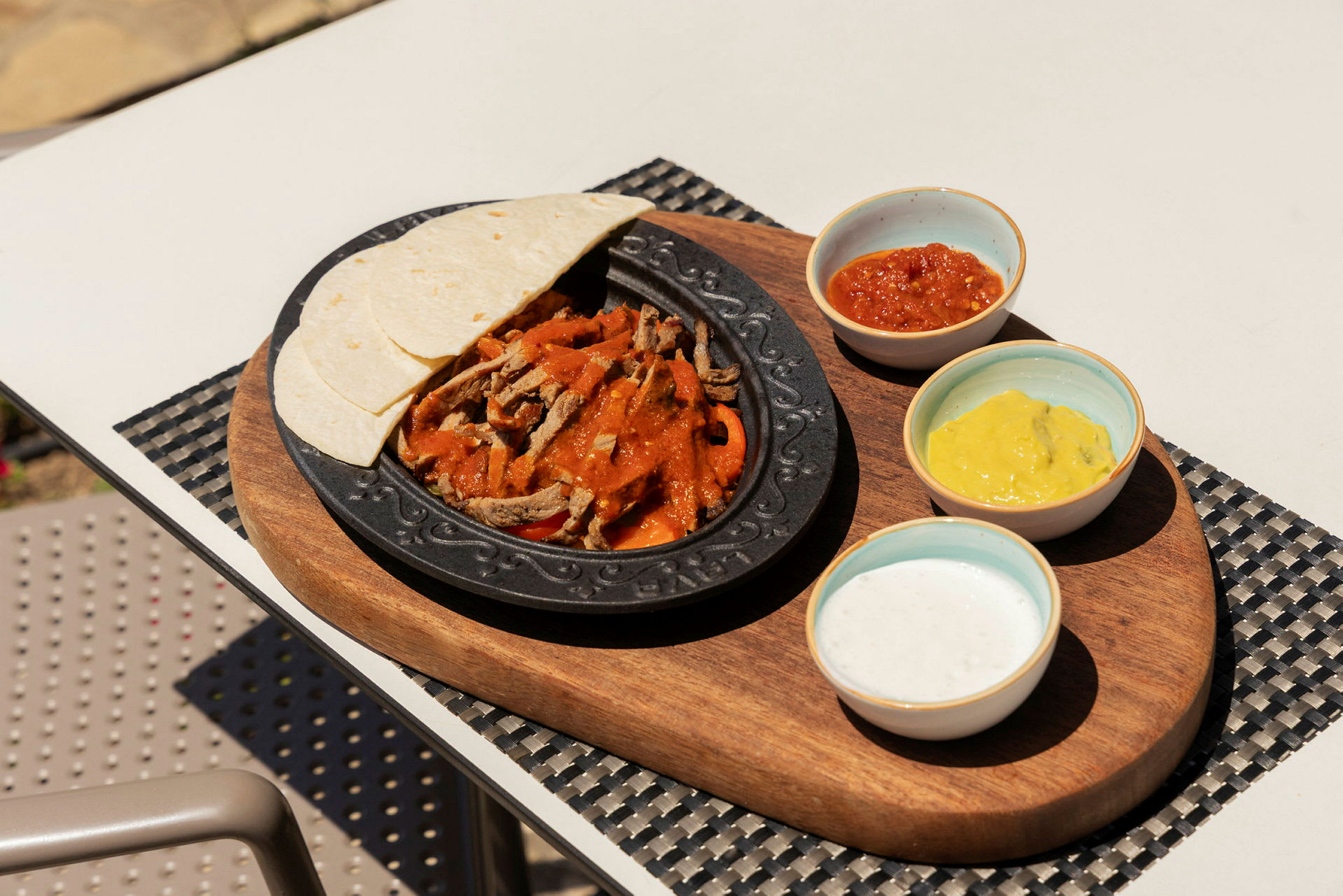 En tallerken med kjøtt, grønnsaker og sauser samt tortillabrød på en trebrikke. (AI-generert tekst)