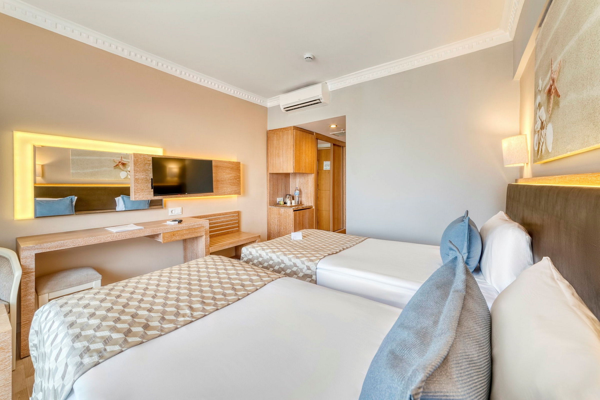 Hotellrom med to enkeltsenger, skrivebord, TV og lys innredning. (AI-generert tekst)