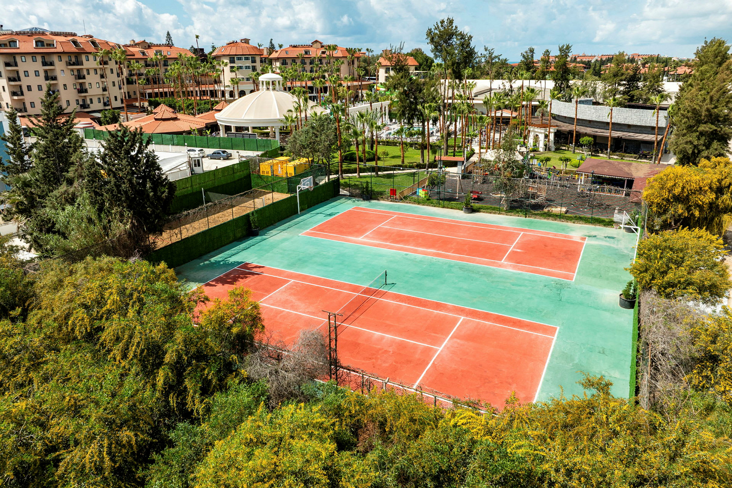 Bilde av to tennisbaner omgitt av grøntområder og bygninger i bakgrunnen. (AI-generert tekst)