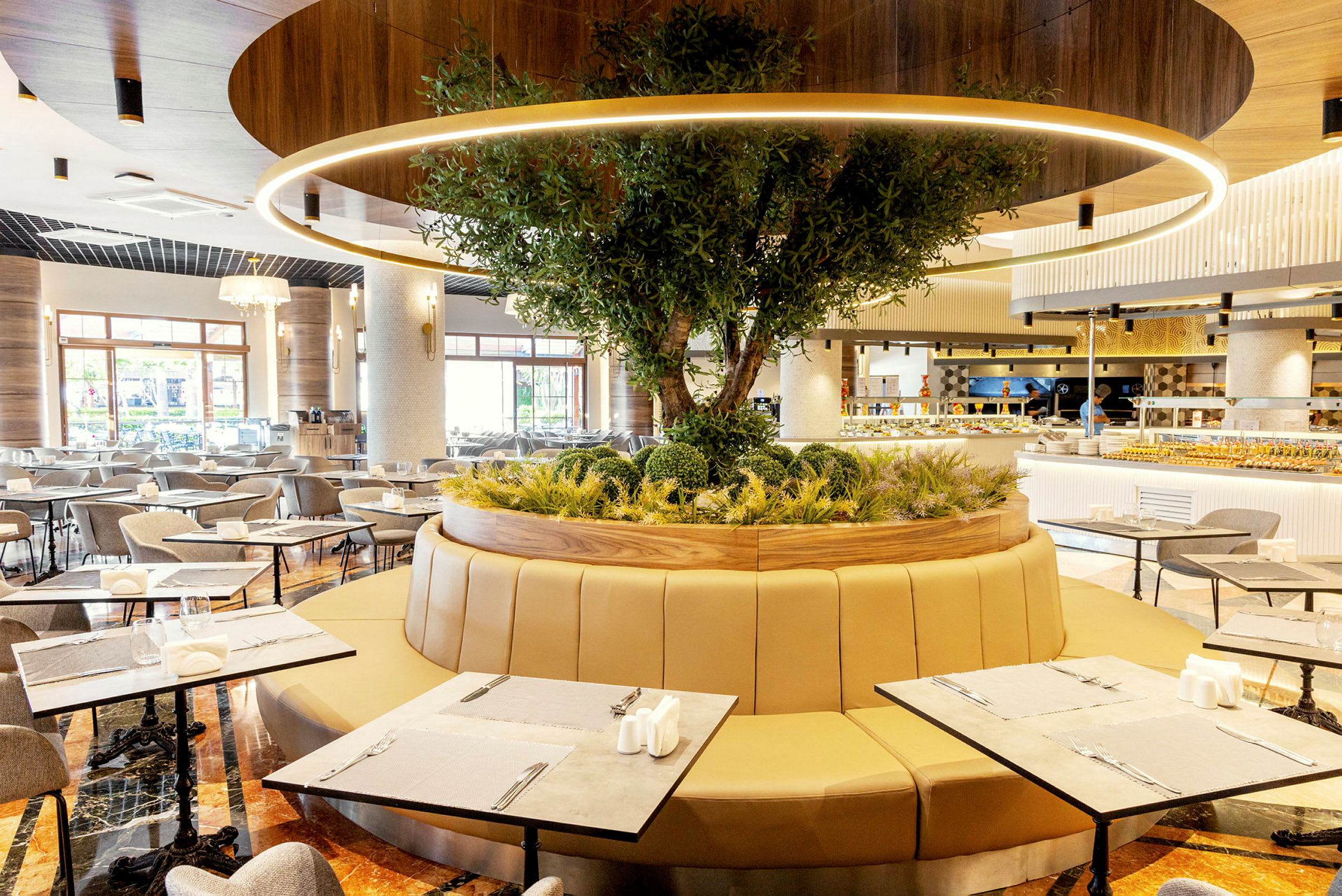 Et moderne restaurantområde med sitteplasser rundt et sirkulært planteområde med et tre. (AI-generert tekst)